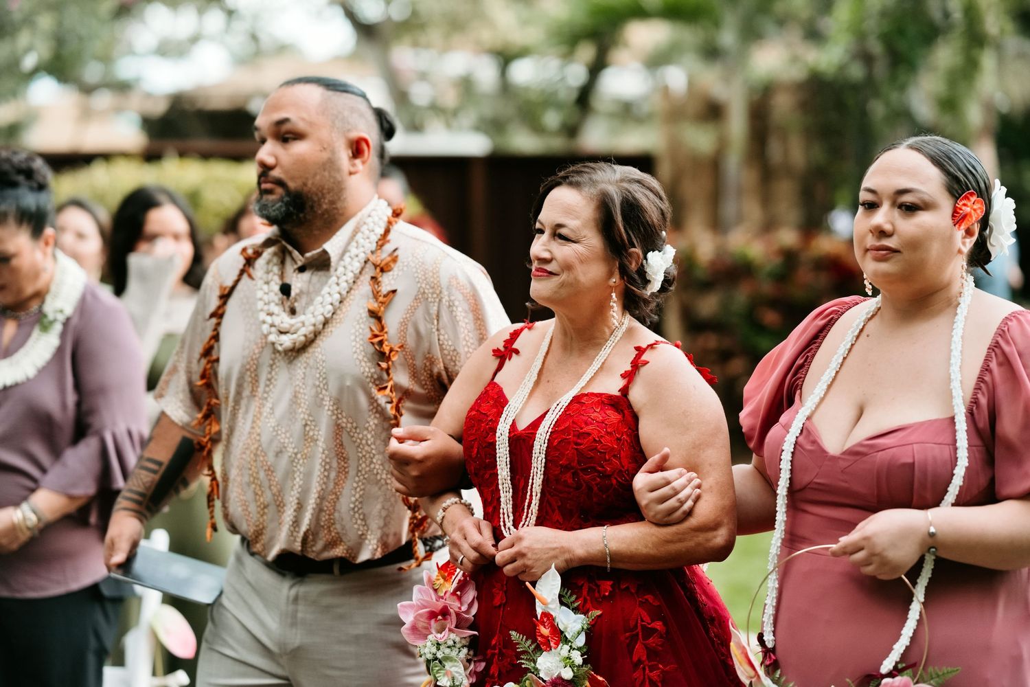 Wedding procession with guests in floral leis and traditional attire walking outdoors at a Hawaiian ceremony.