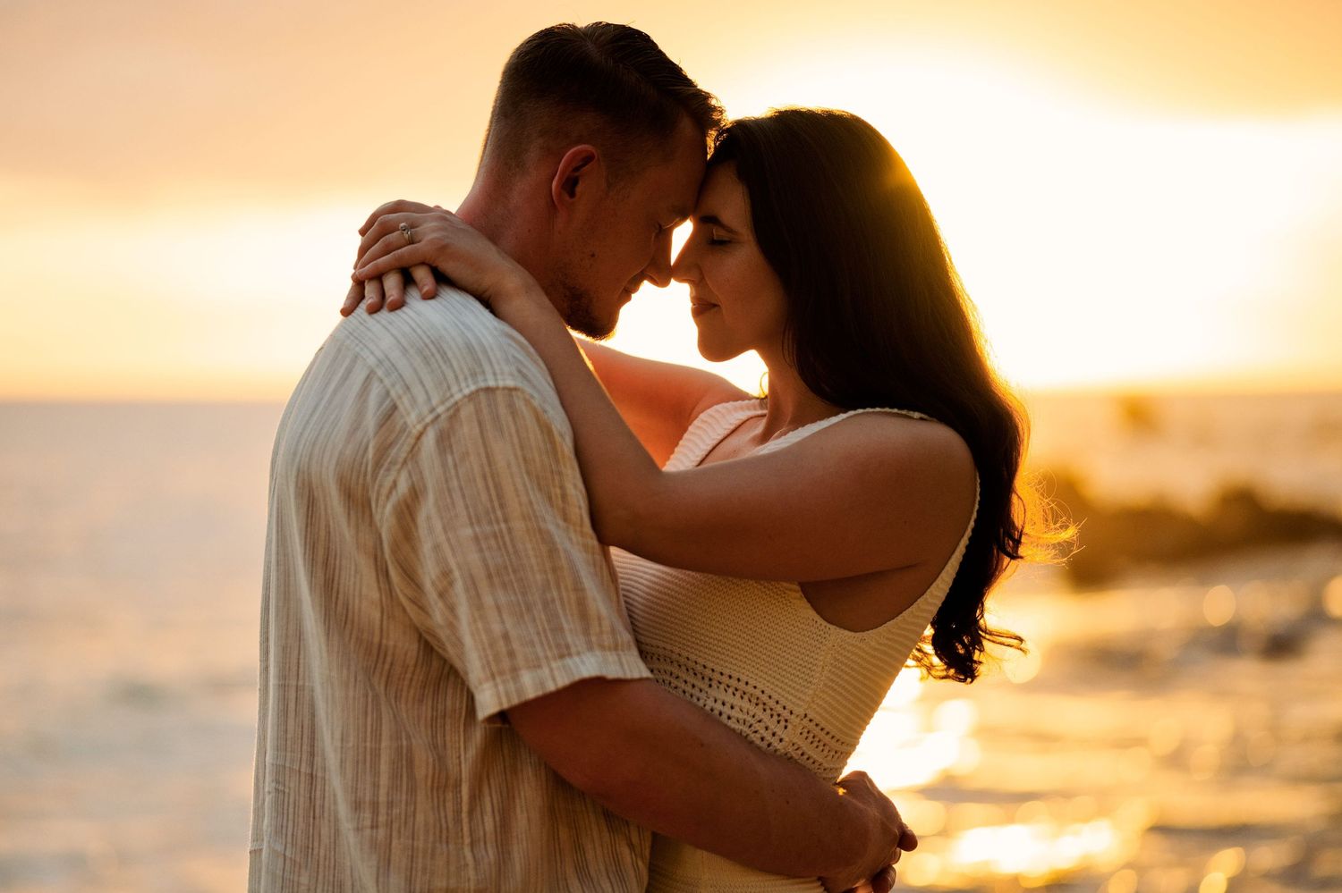 Romantic couple embracing at sunset on a beach with golden ocean light behind them.