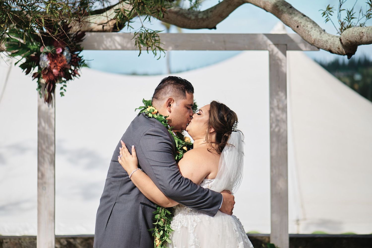 Romantic wedding couple shares intimate moments under a tree arch with decorative floral arrangements.