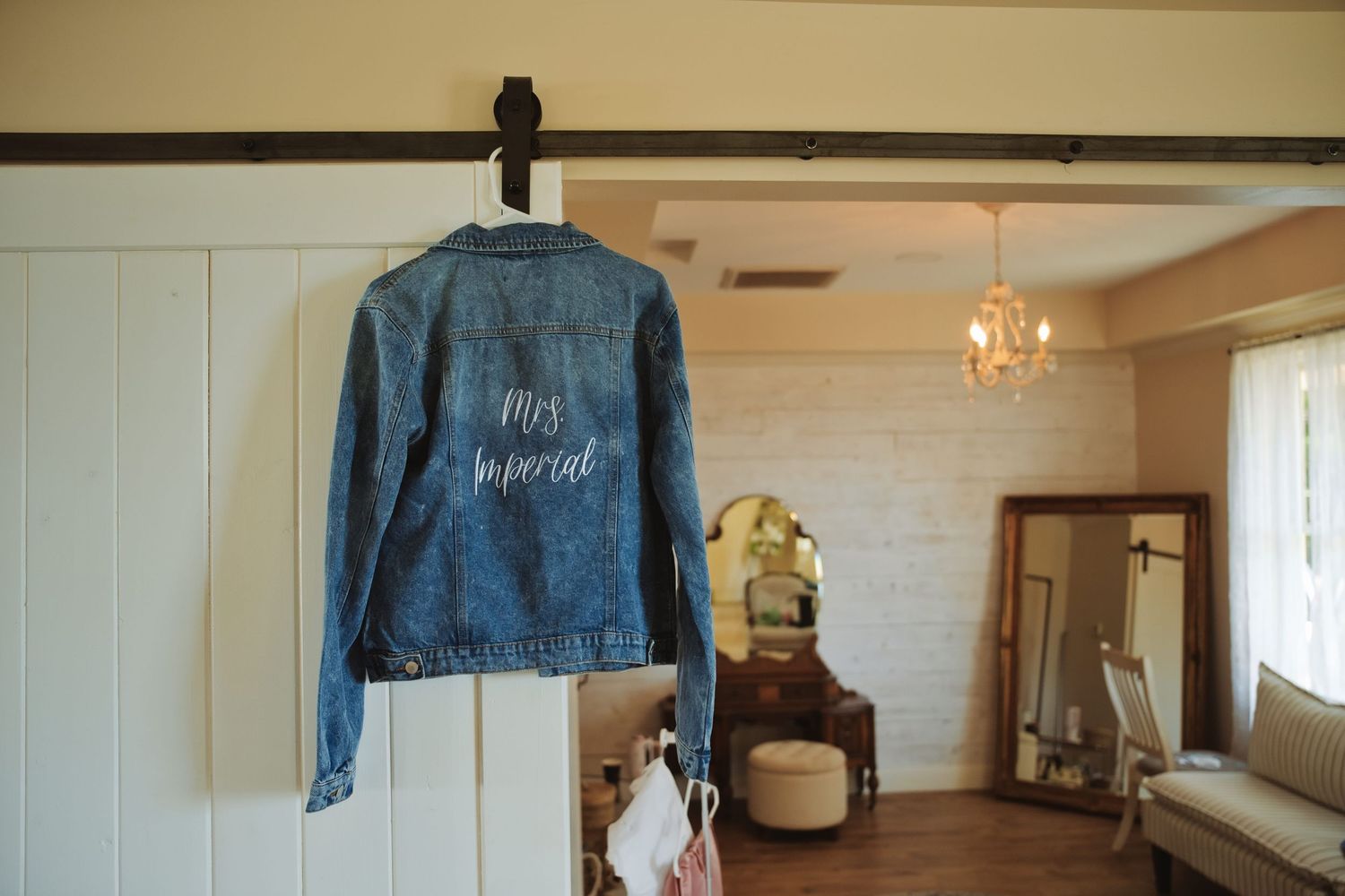 A custom denim jacket reading Mrs Imortal hangs on a hook in a bright bridal getting ready room.
