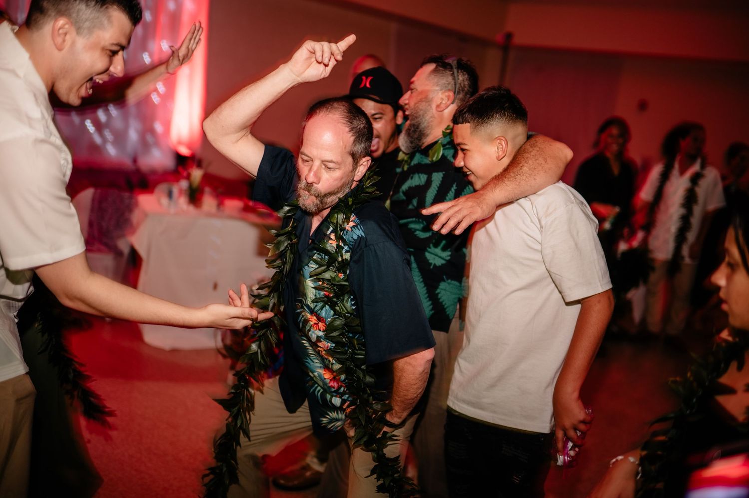 Wedding guests dance and celebrate with traditional Hawaiian leis at reception party.