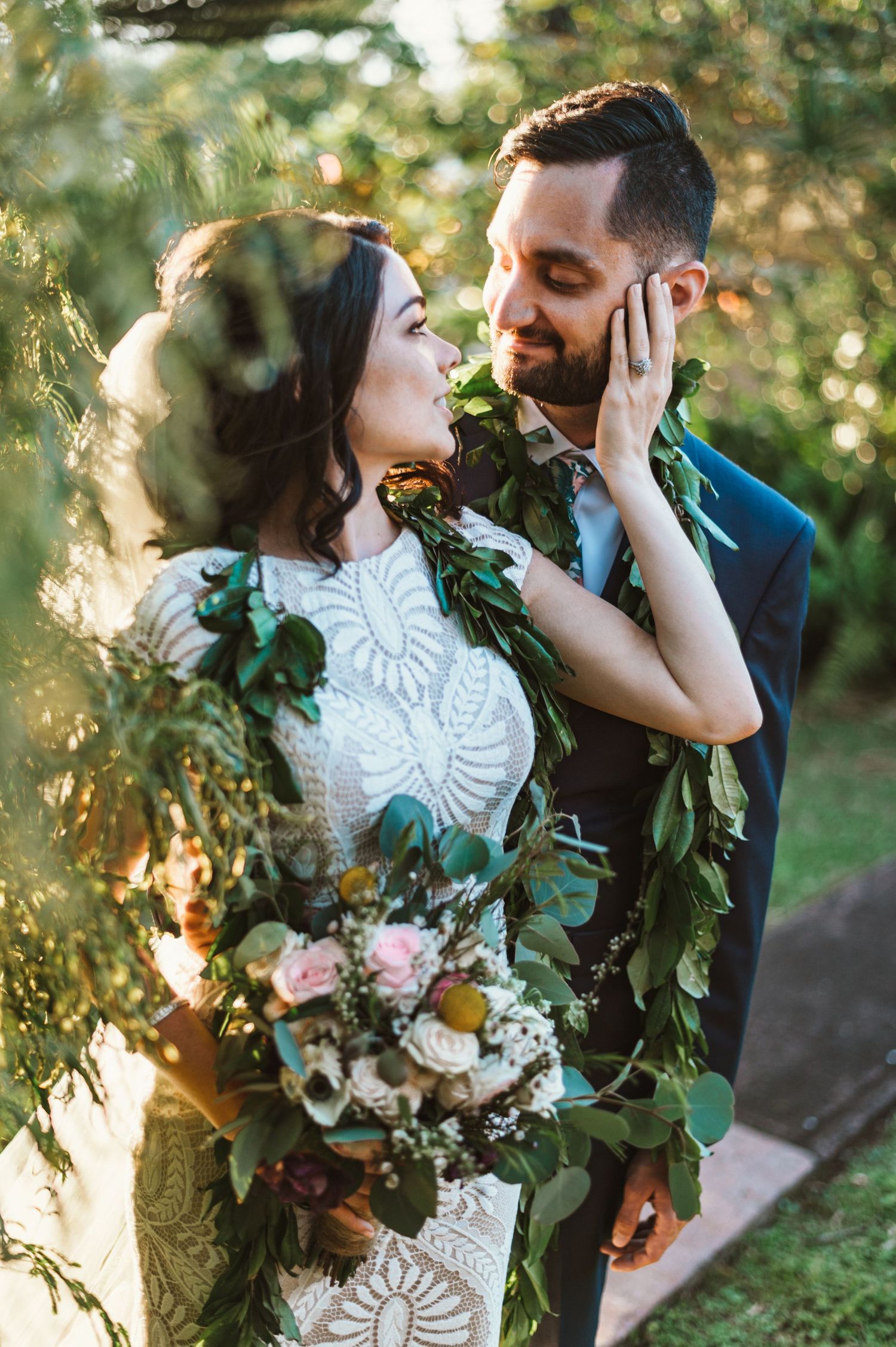 Intimate wedding portraits captured through sunlit trees with floral bouquet and greenery garlands.