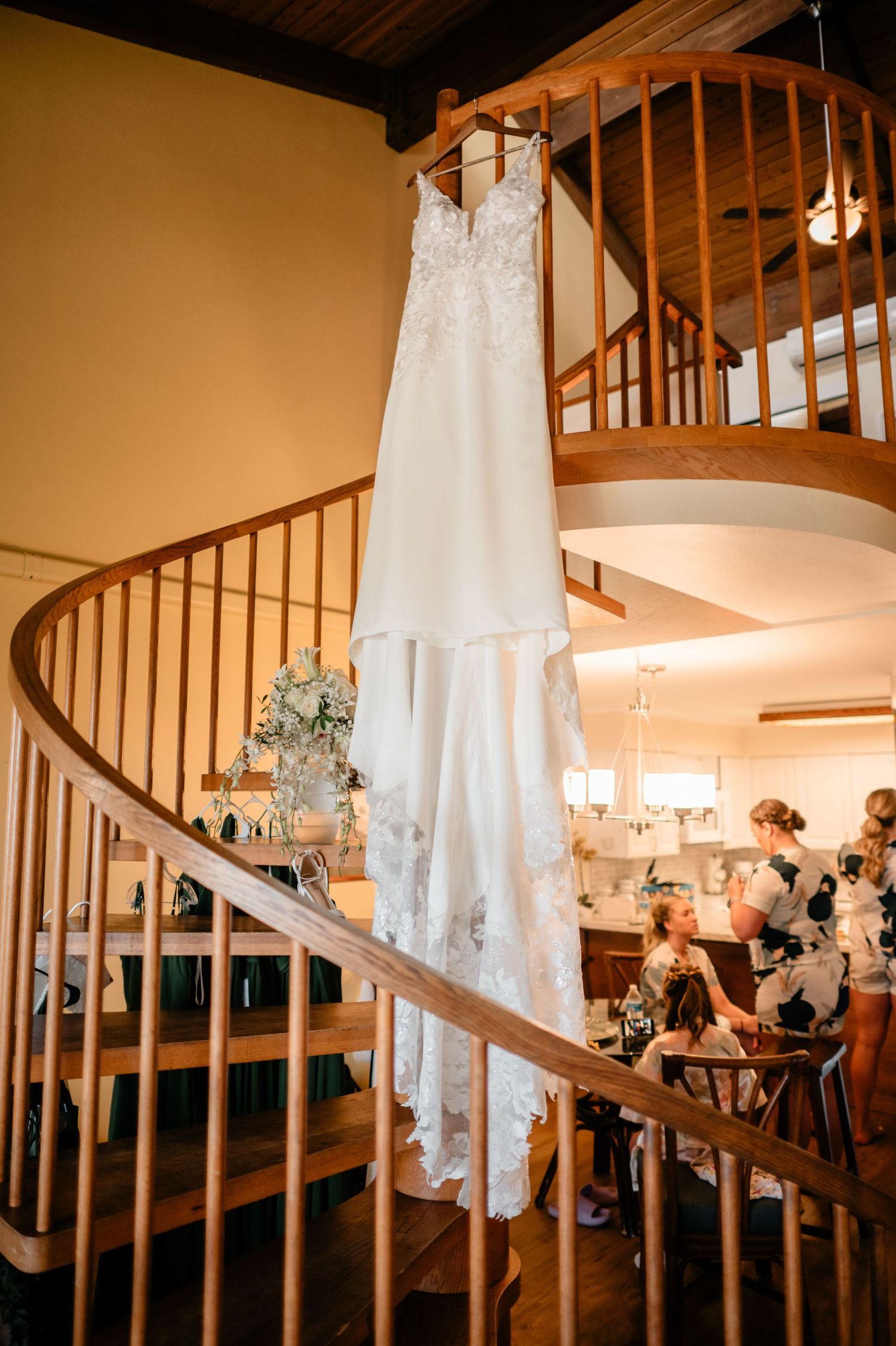 An elegant white lace wedding dress hangs on a curved wooden staircase railing.