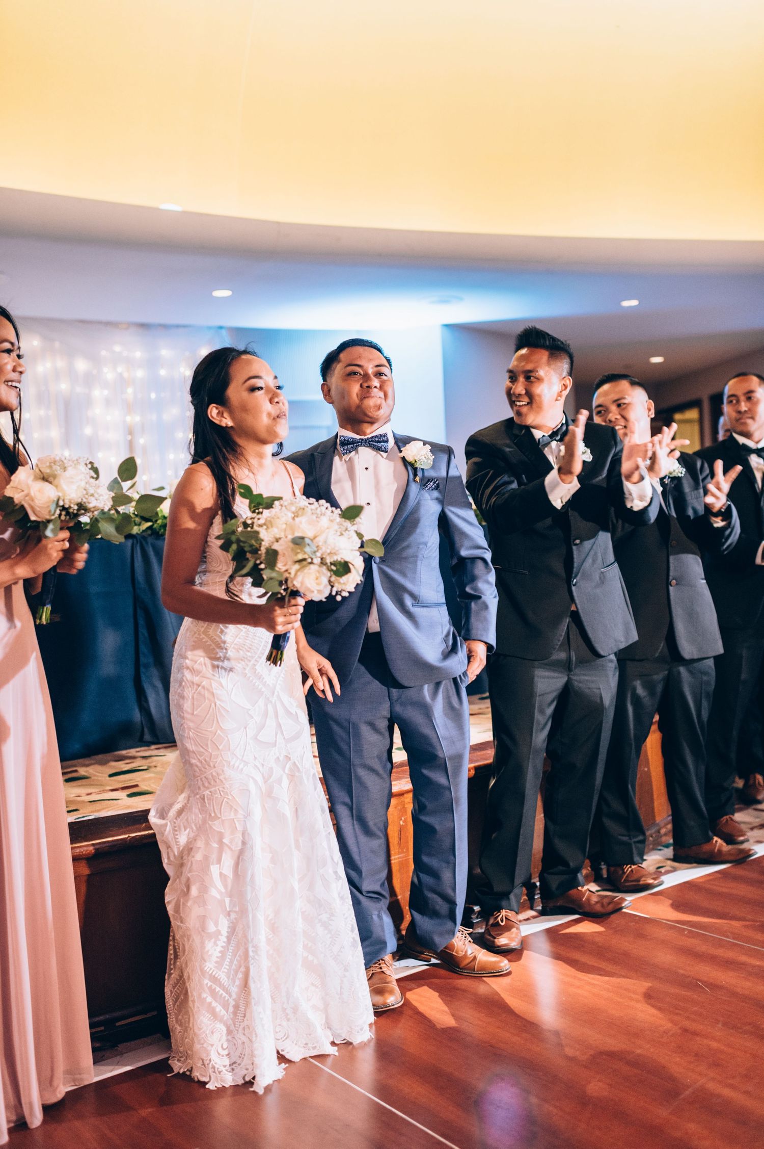 Wedding party lines up in formal attire on hardwood floors during reception celebrations.