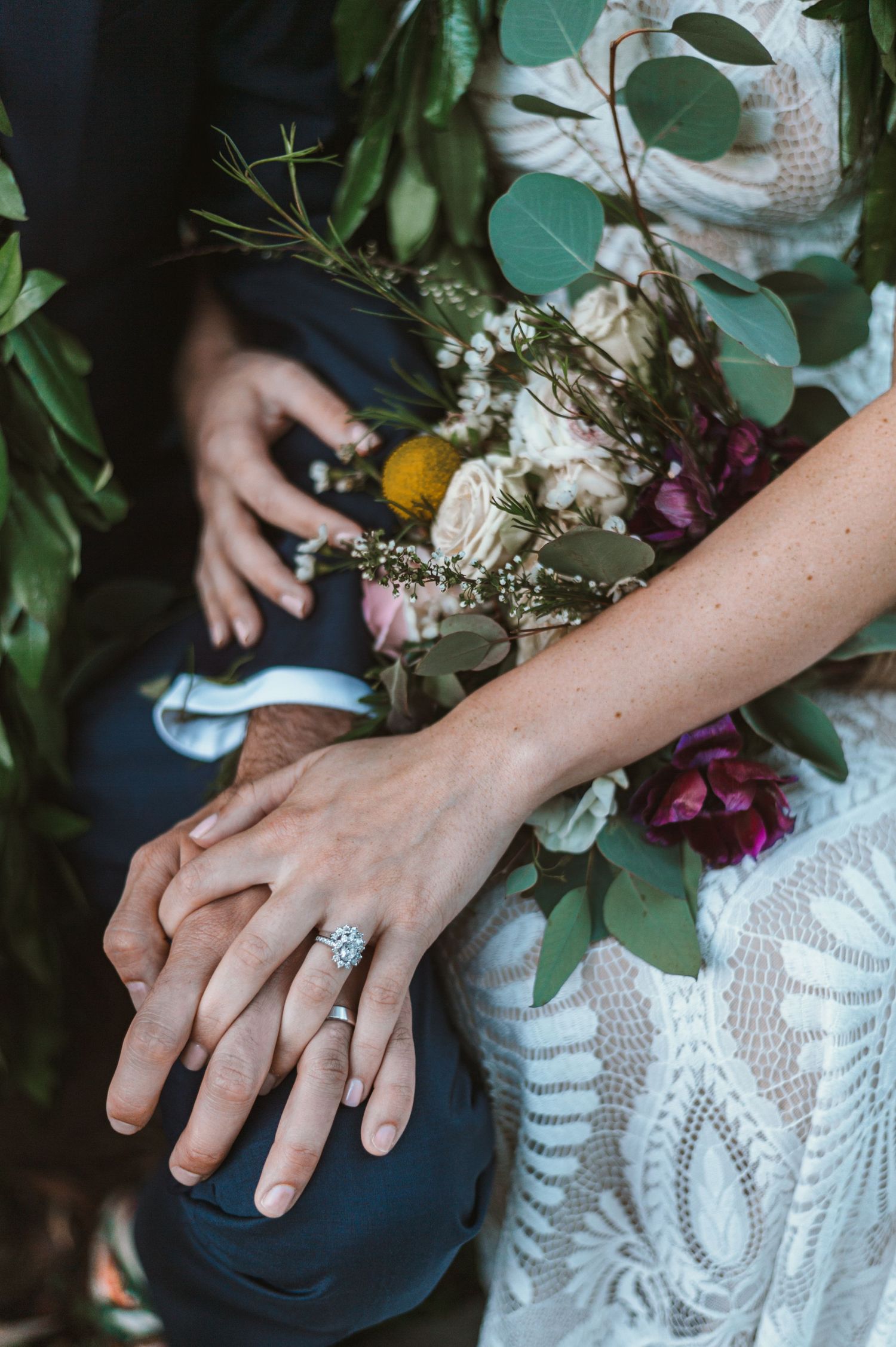 Close-up of hands with engagement ring and wedding bouquet featuring eucalyptus leaves and mixed flowers.
