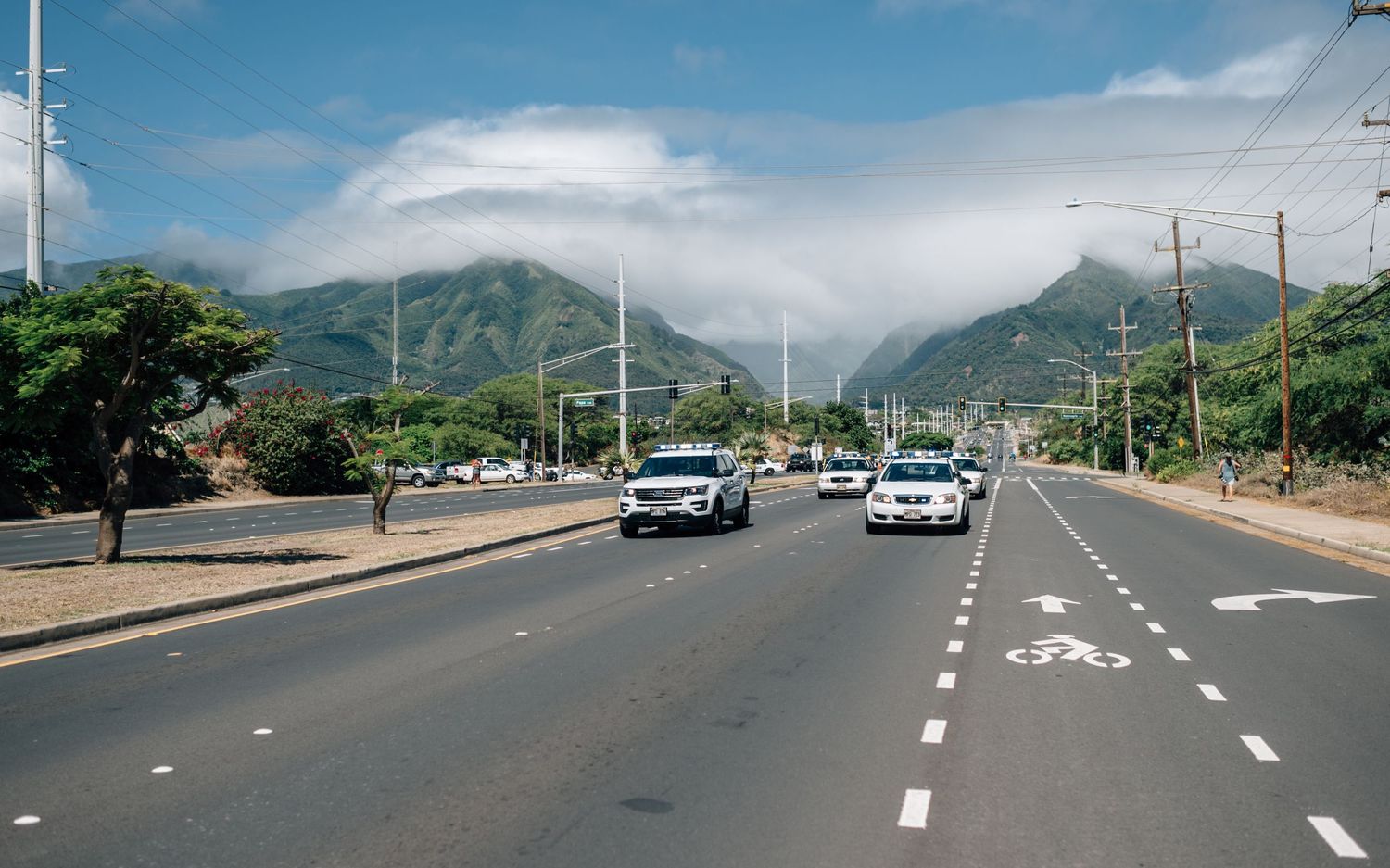 Empty road with lane markings leads toward mountains under bright blue sky with scattered clouds.