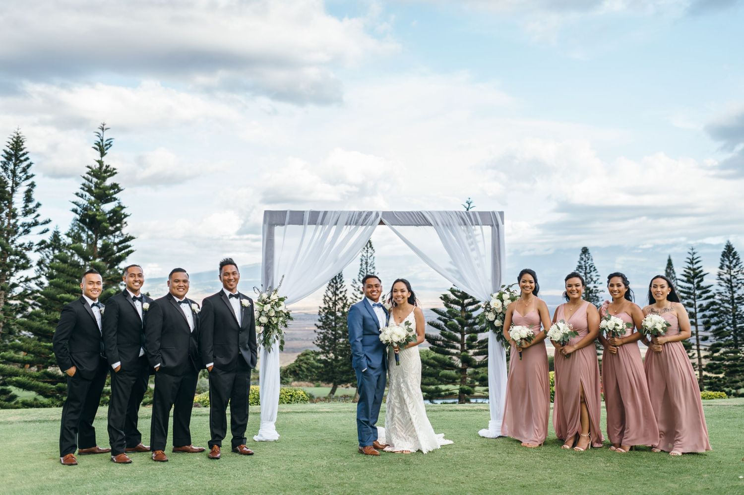 Wedding ceremony setup with white arch and chairs against mountain landscape.