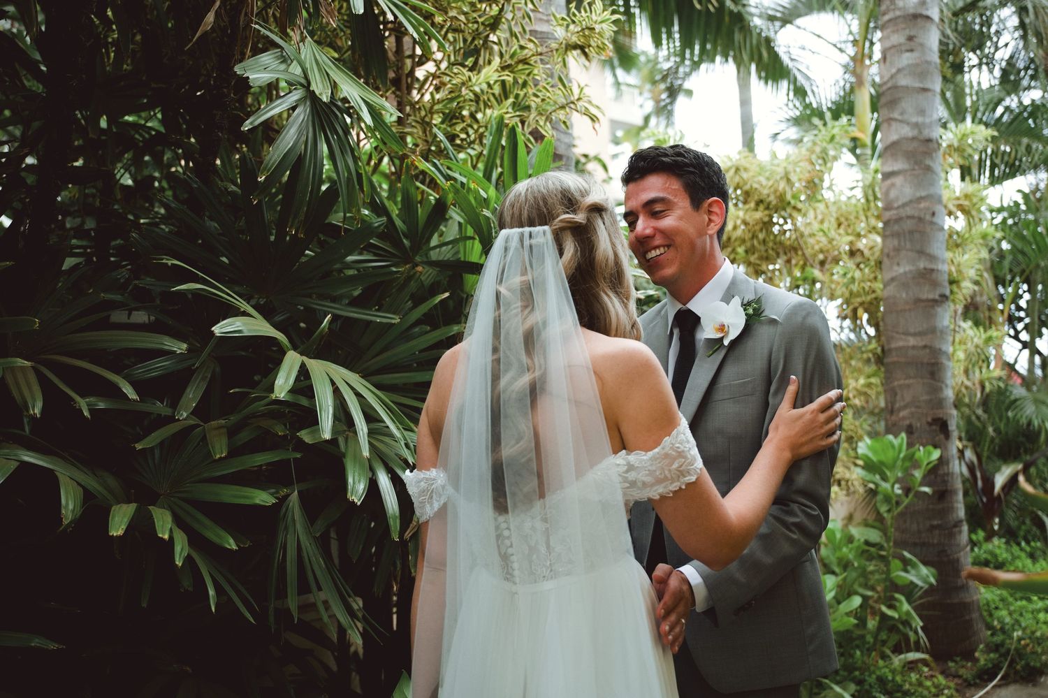 Bride and groom share a joyful first look moment surrounded by lush tropical greenery on their wedding day.