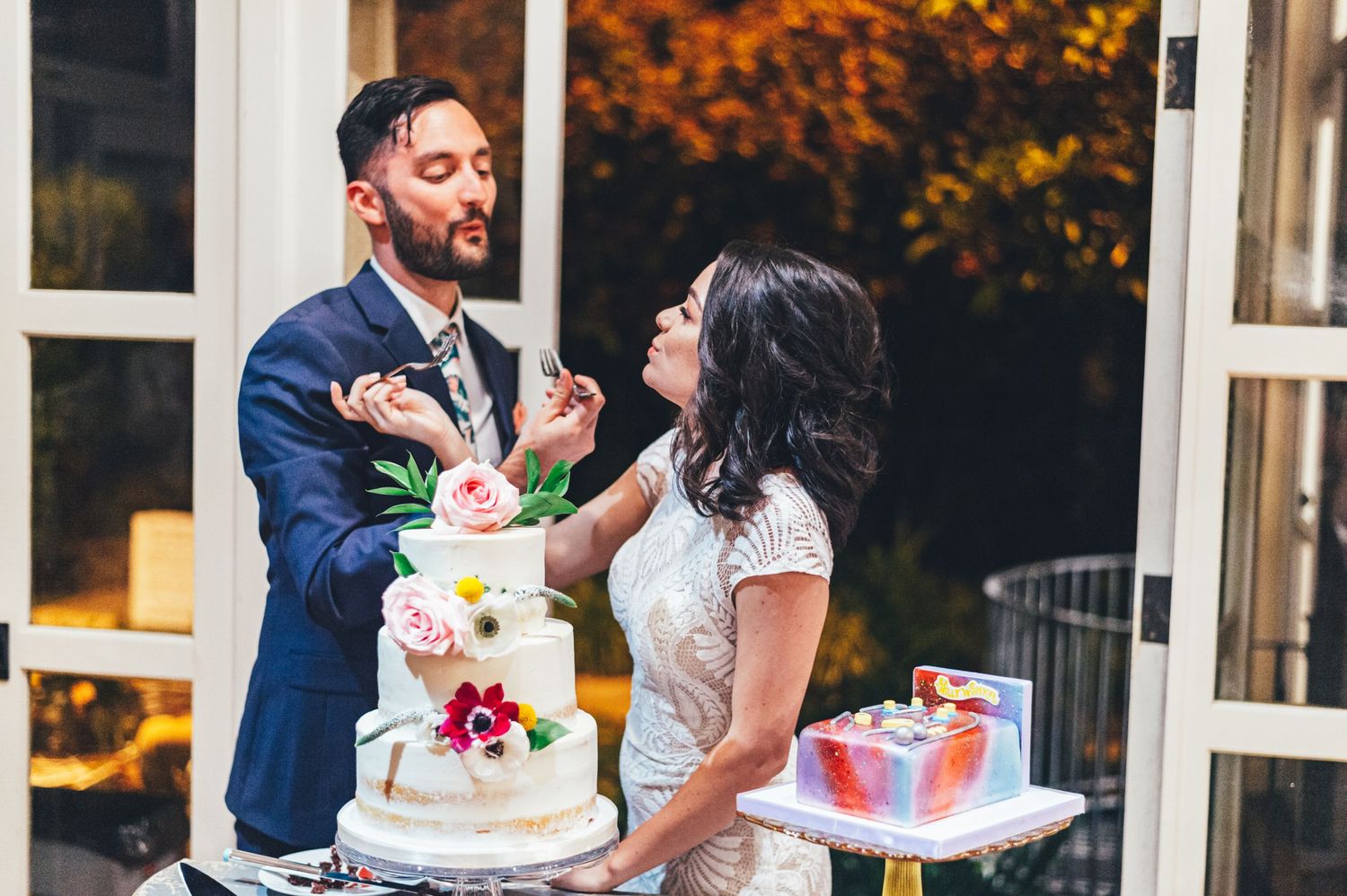 Newlyweds feeding each other wedding cake at an outdoor reception venue.