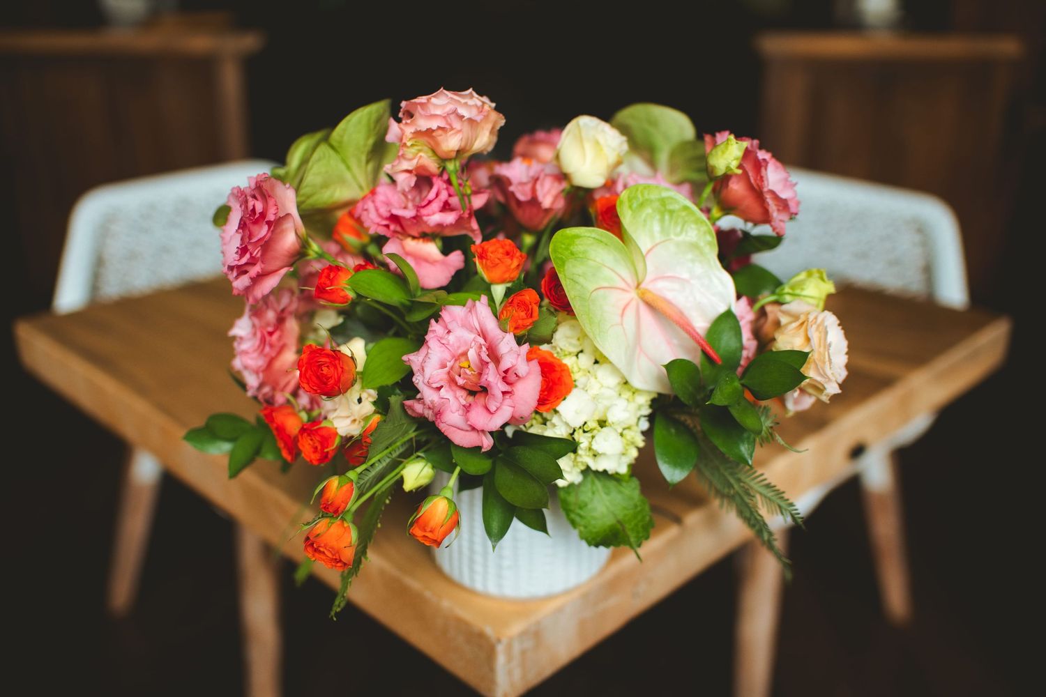 Vibrant pink and orange floral arrangement in a white vase on a wooden table.