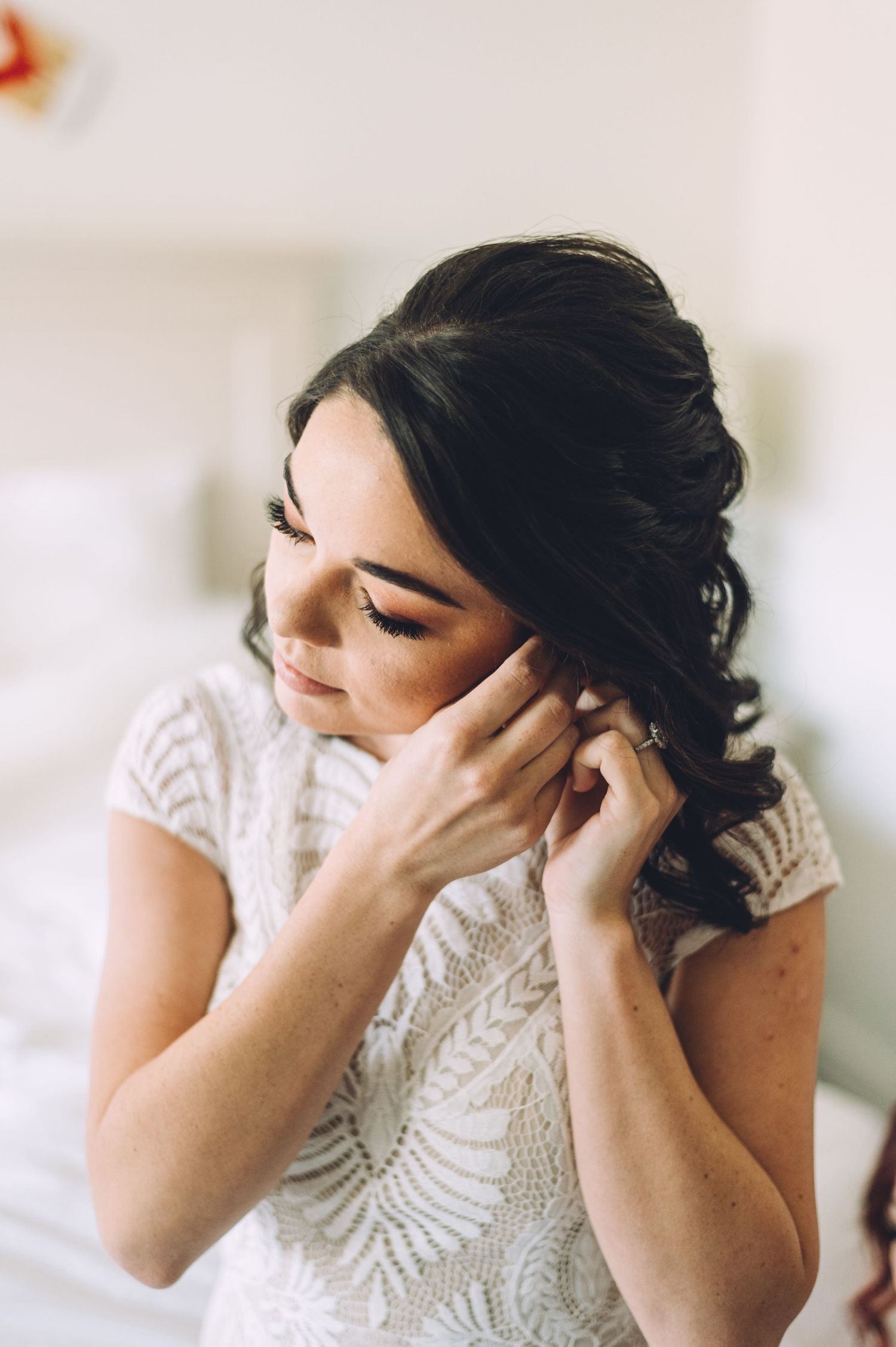 Side profile of someone putting on earrings while wearing a detailed lace dress.