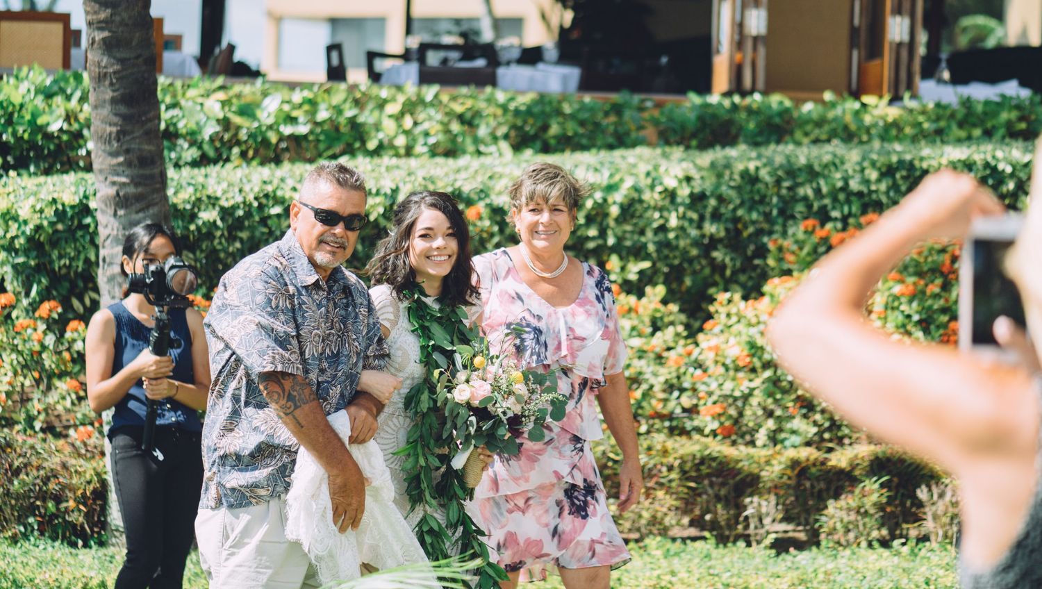 Wedding party members in burgundy dresses and floral attire celebrate joyfully outdoors.