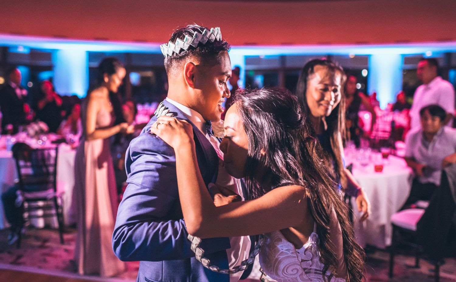 Wedding celebration with couples dancing under vibrant red and blue mood lighting.