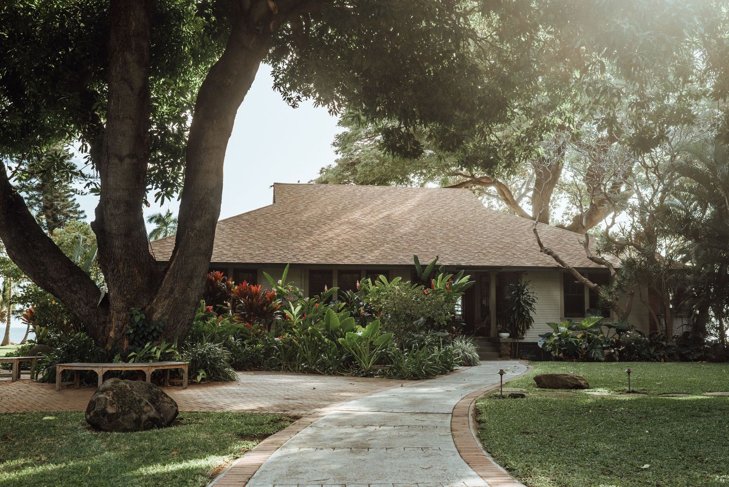 Tropical bungalow with lush gardens, stone pathway, and large shade trees in a serene Hawaiian resort setting.