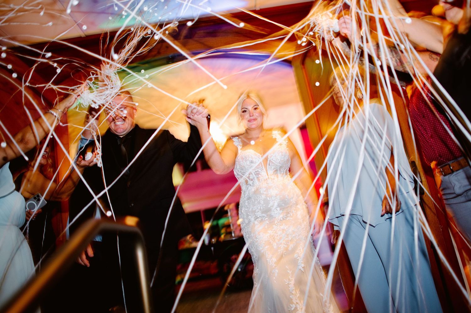 Bride in lace gown dancing with streamers and sparklers at a vibrant wedding reception celebration.