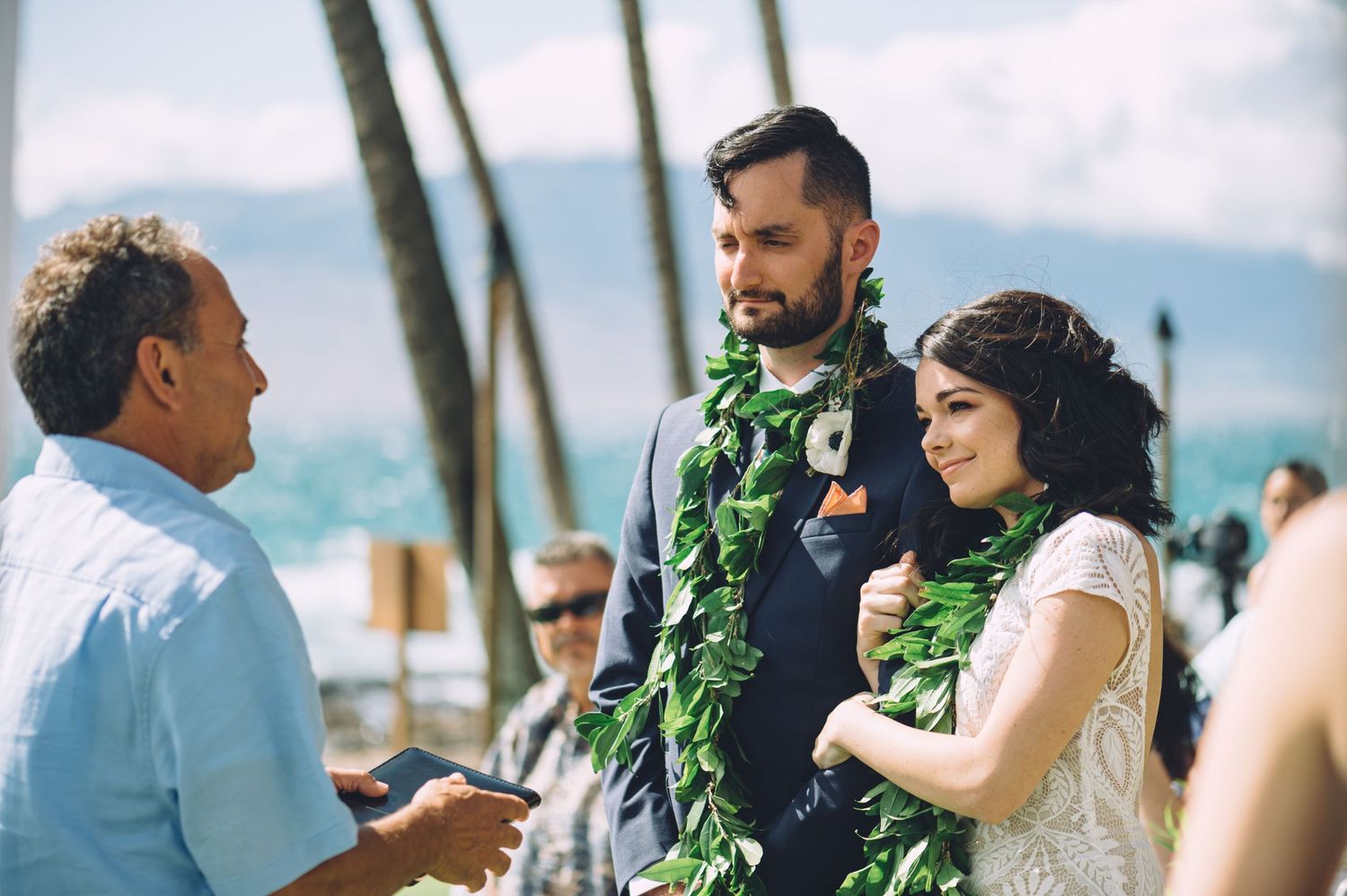 Tropical outdoor wedding ceremony with guests and palm trees in background.