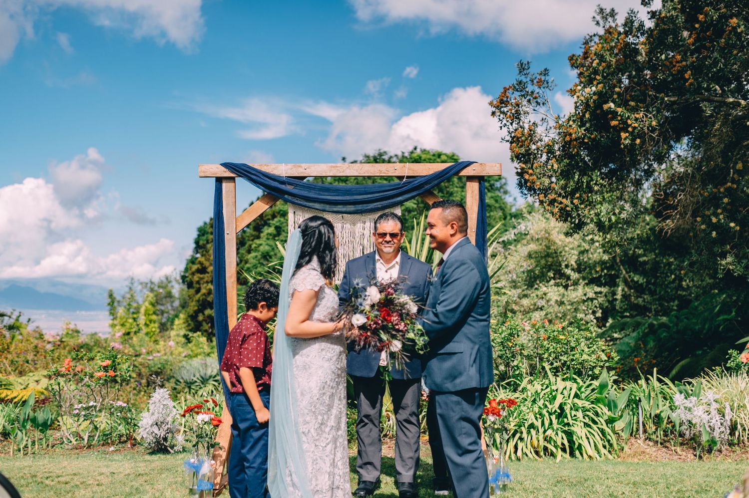 Outdoor wedding ceremony in a lush garden setting with decorative elements and guests in attendance.