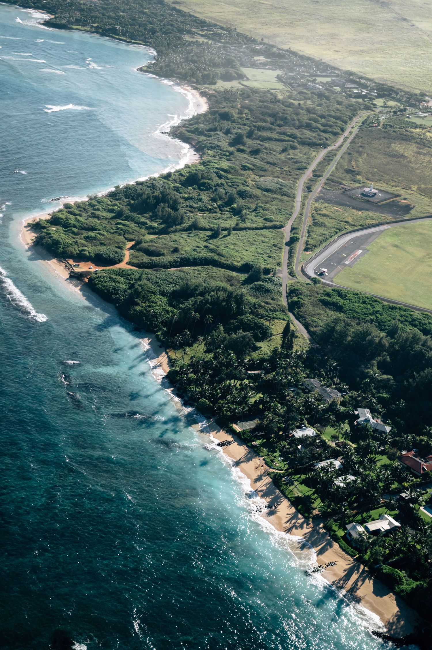 Aerial perspective of a scenic coastline with beaches, cliffs and winding roads.