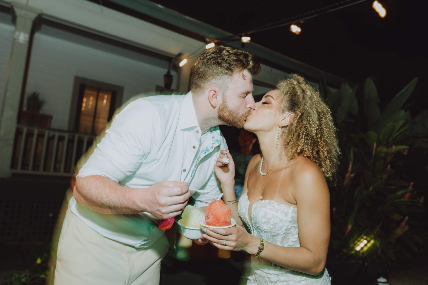 A romantic wedding reception moment with a couple sharing watermelon under twinkling lights.