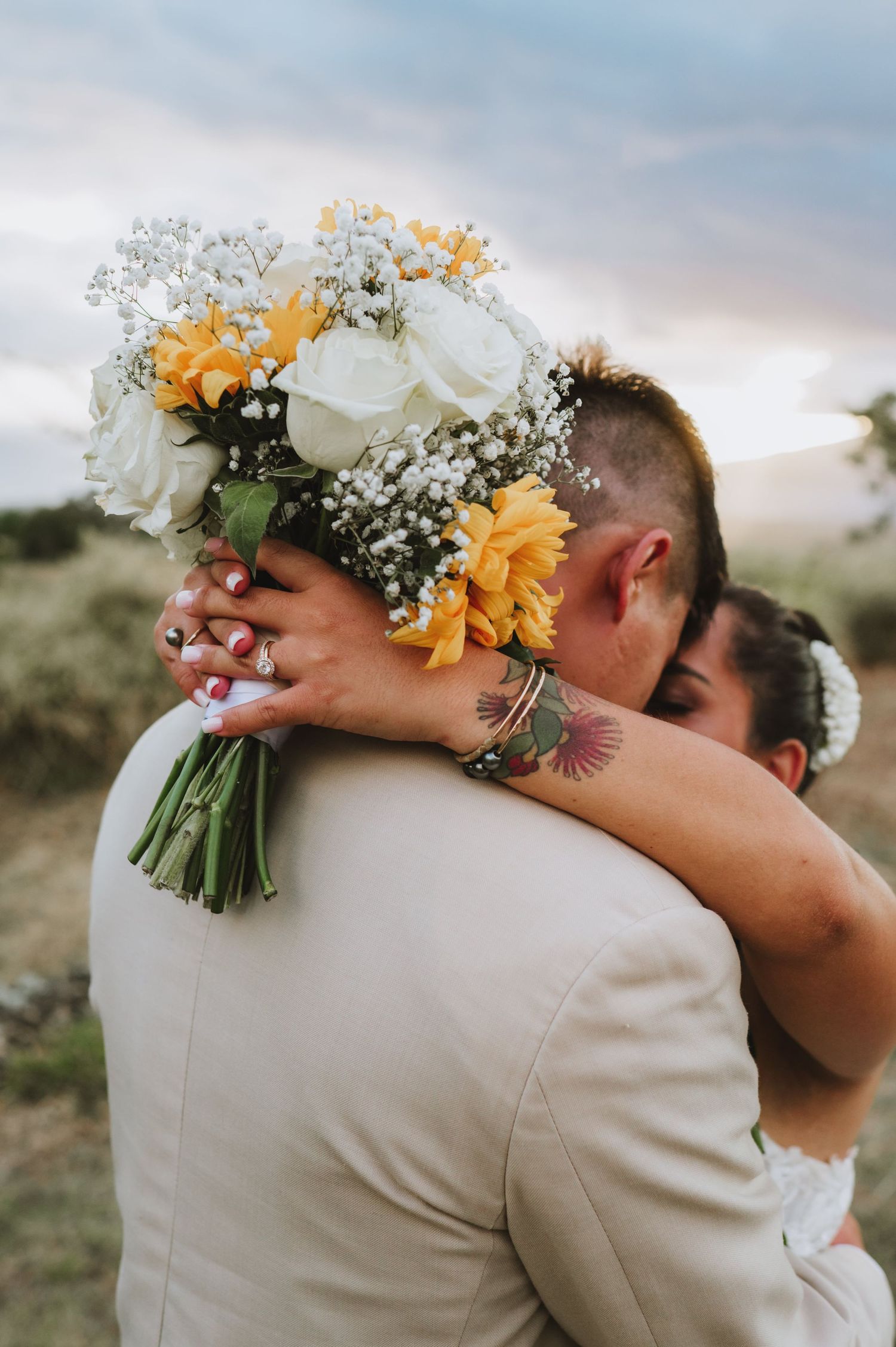 Close-up of embrace with white and yellow floral bouquet featuring roses and baby's breath.
