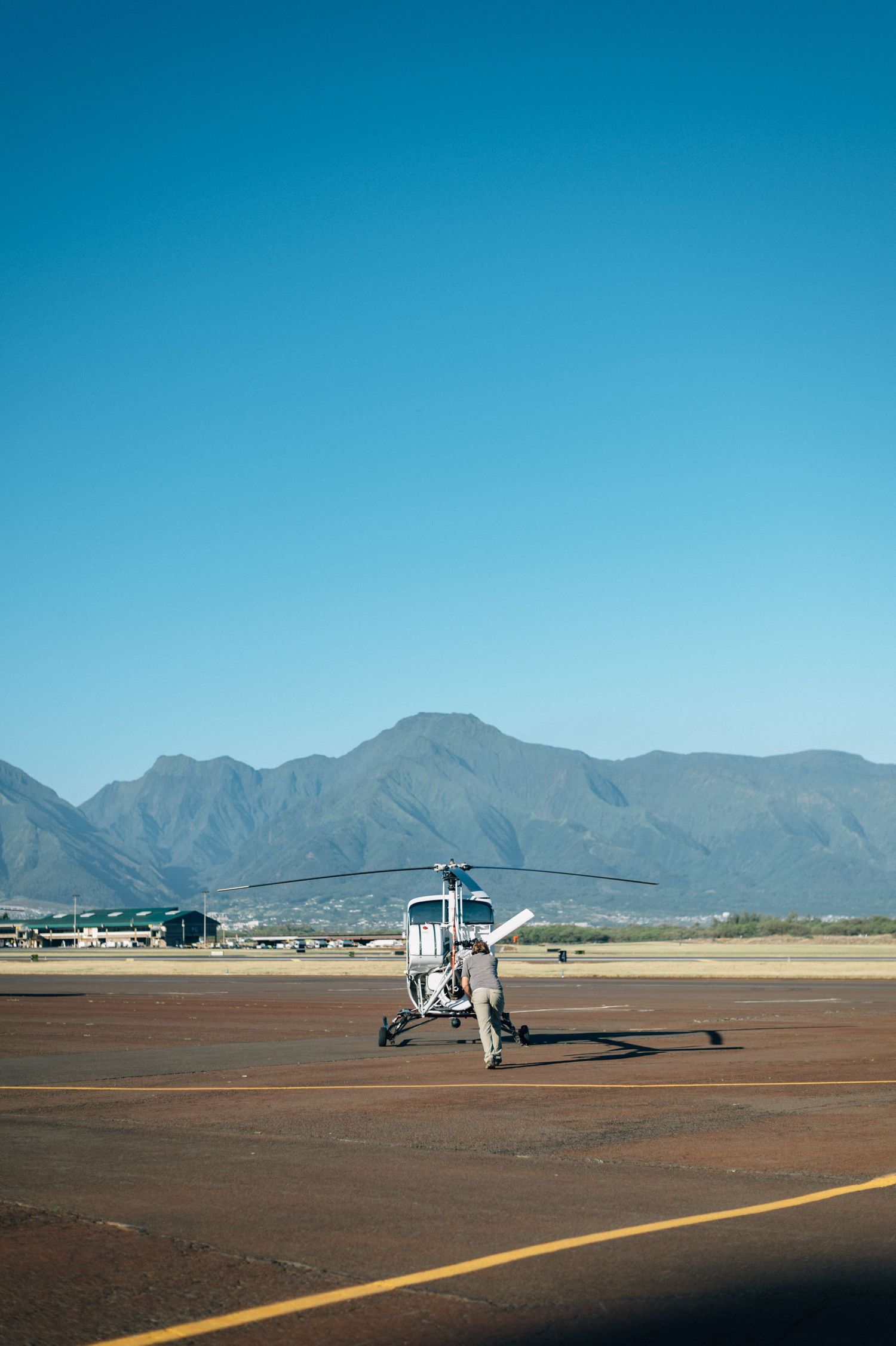 Helicopter stationed on desert airstrip with mountain range visible in distance.