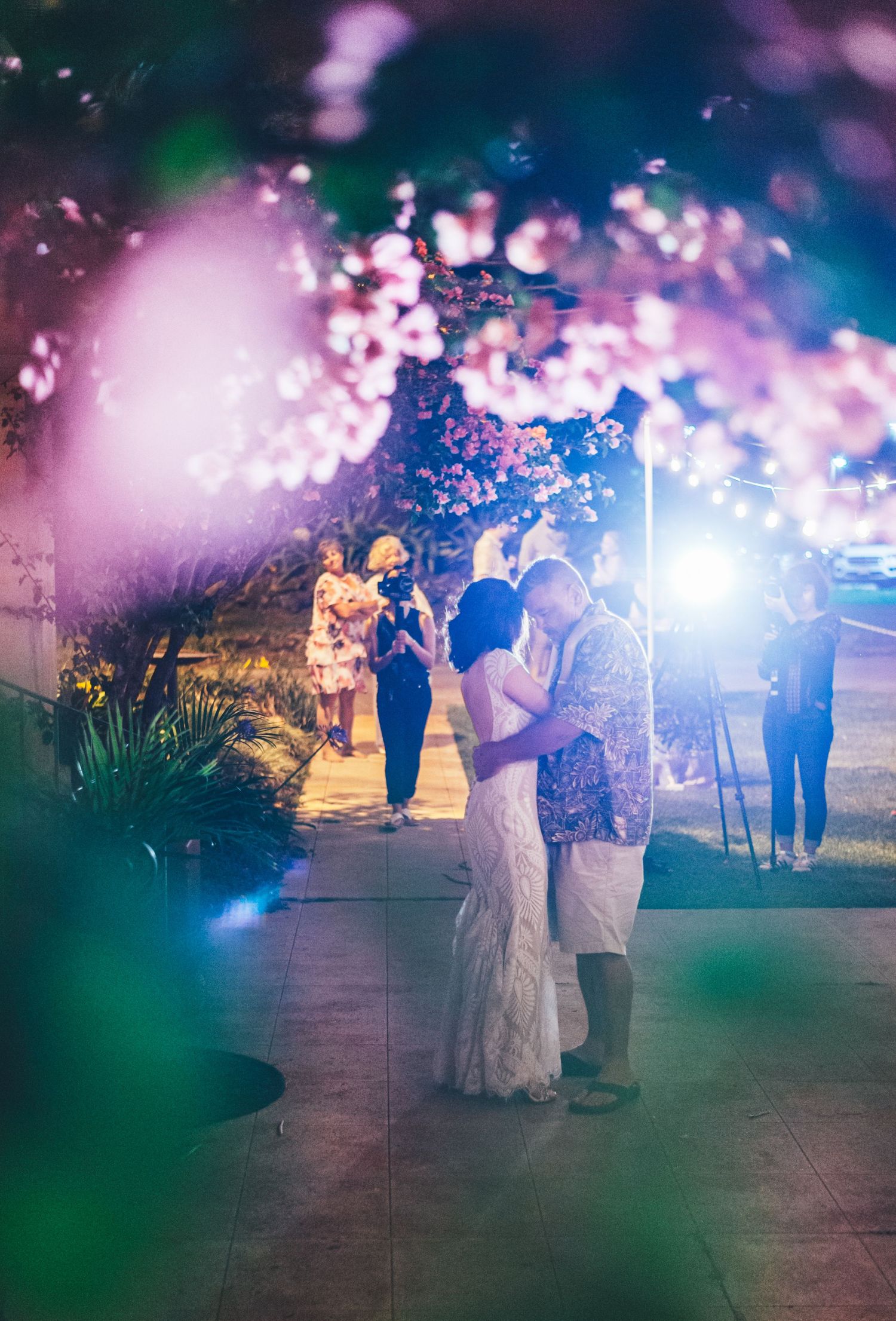 Romantic evening dance under colorful lights and bokeh effects at an outdoor wedding reception.