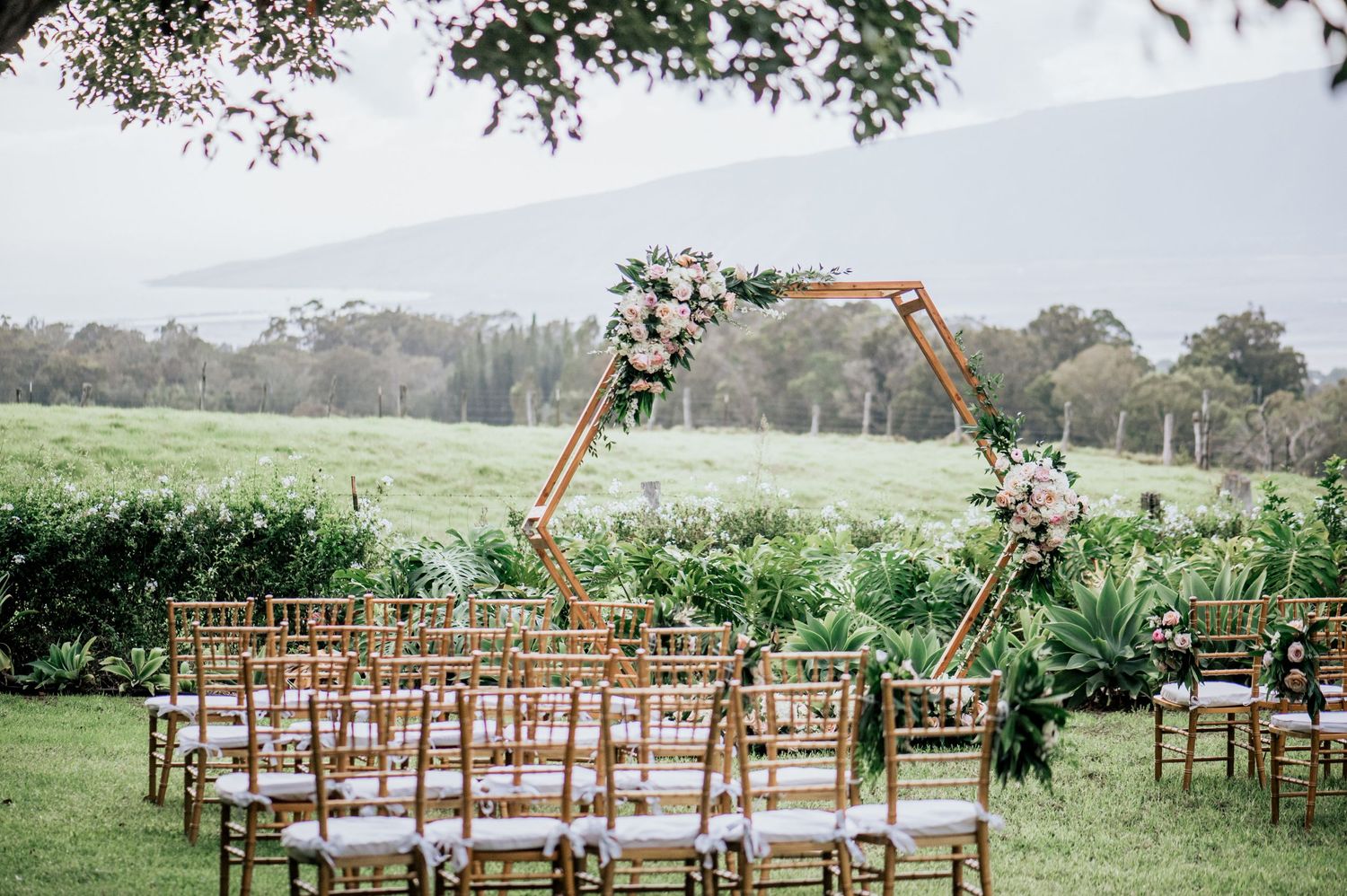 Outdoor wedding venue setup with wooden chairs arranged in rows on a grassy field.
