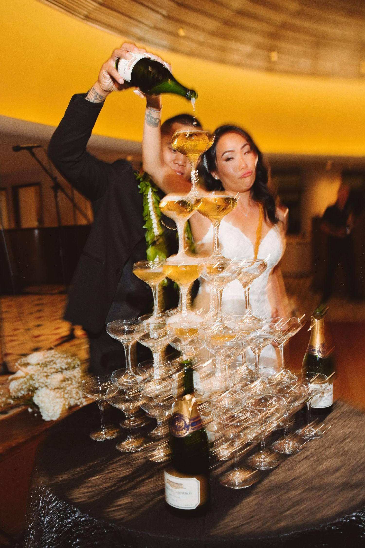 Bride and groom pouring champagne tower at wedding reception celebration.