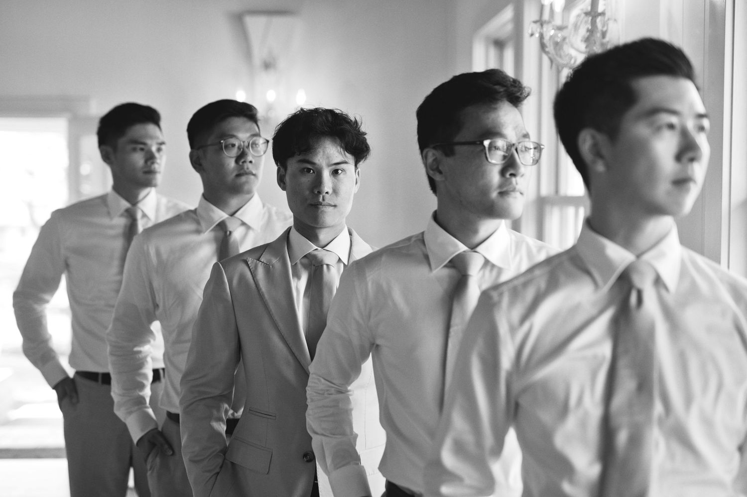 Five young men in dress shirts and ties pose in a line for a black and white wedding party photo.