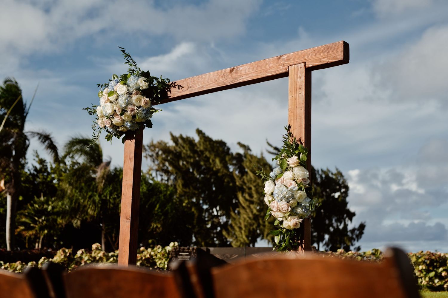 Rustic wooden wedding arch adorned with white floral arrangements outdoors under a blue sky.