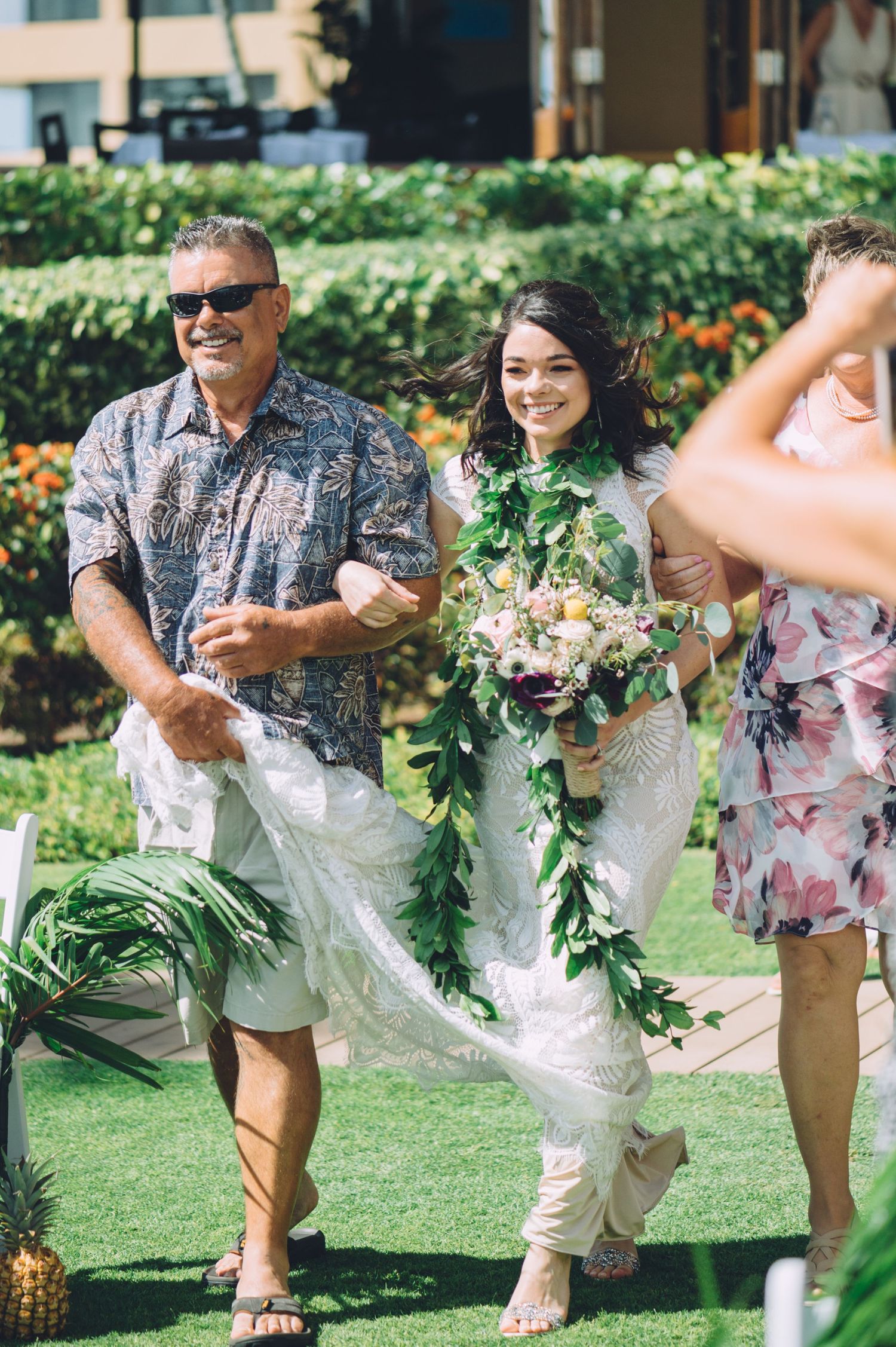 Wedding party members wearing floral prints and leis celebrate on a tropical lawn.