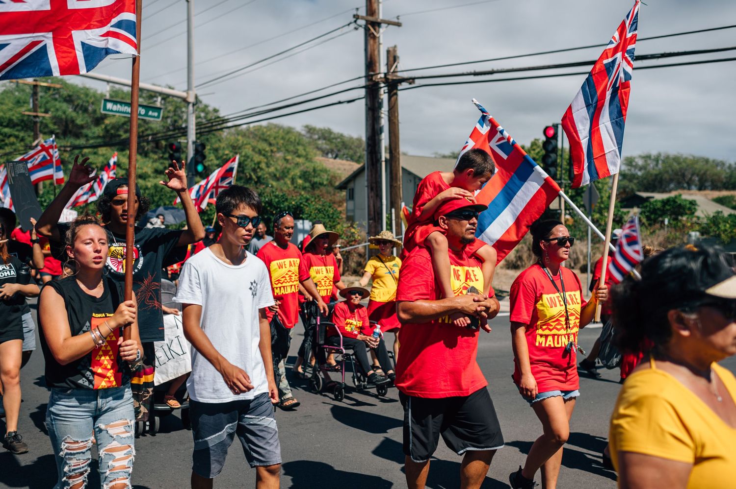 Protesters carrying Hawaiian state flags gather for demonstration under cloudy skies.