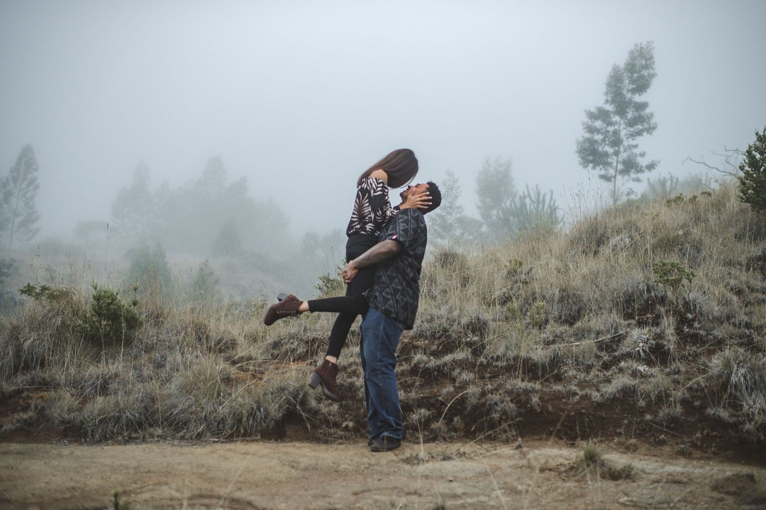Silhouettes of a couple embracing on a misty hillside.