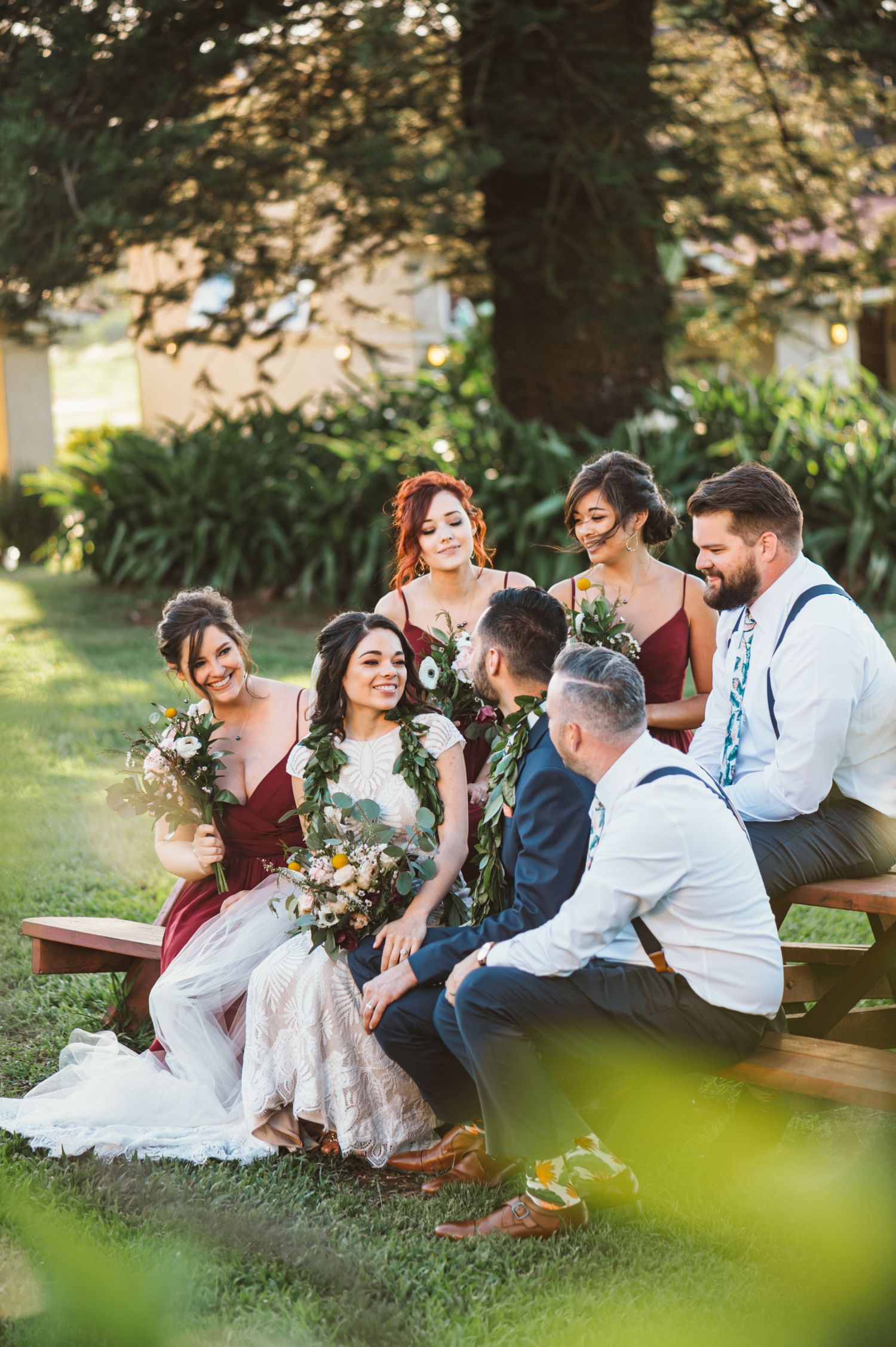Wedding party relaxes on grass sharing candid laughs during outdoor photo session.