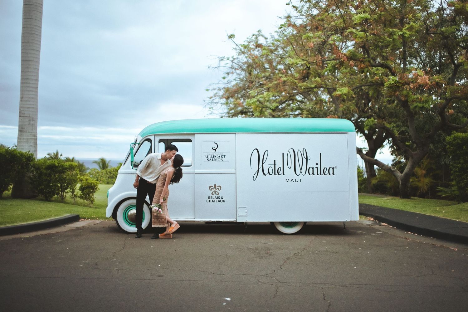 Couple embracing beside a mint green Hotel Wailea branded vintage van in Maui, Hawaii.