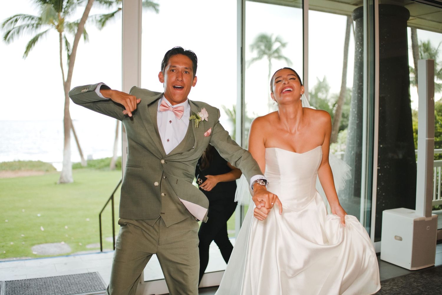 Joyful bride and groom in wedding attire celebrating their entrance at a tropical outdoor venue.