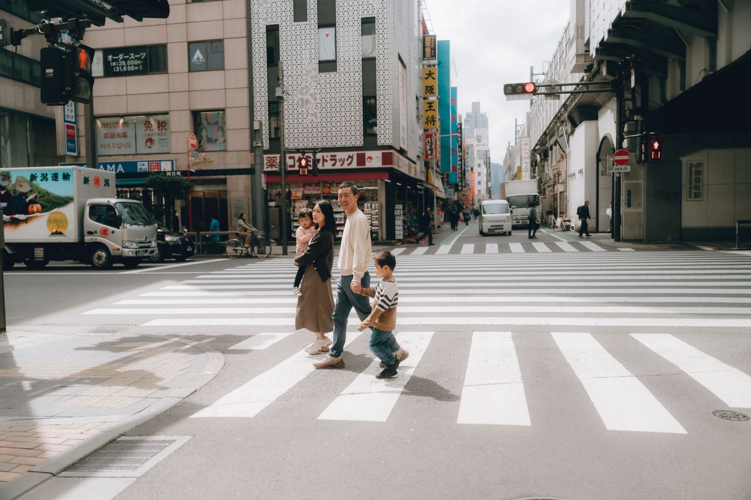 Family crossing a zebra crosswalk on a busy urban street in Japan, with city buildings in the background in Ueno, Tokyo.