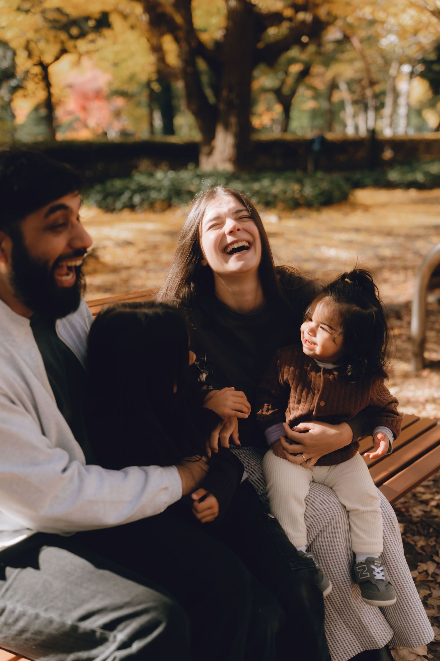 Happy family laughing together on a park bench surrounded by autumn foliage in Hibiya park, Tokyo.