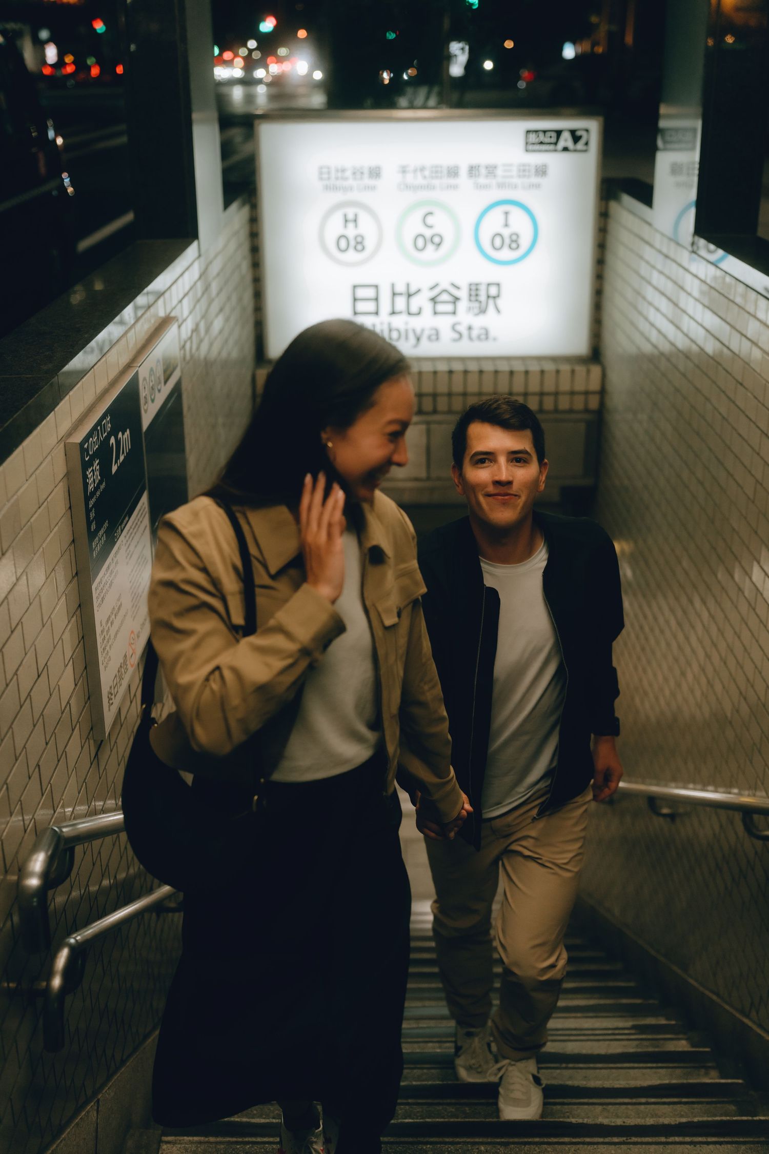 Couple holding hands on stairs at Hibiya Station in Tokyo, Japan at night, smiling and enjoying their time together.