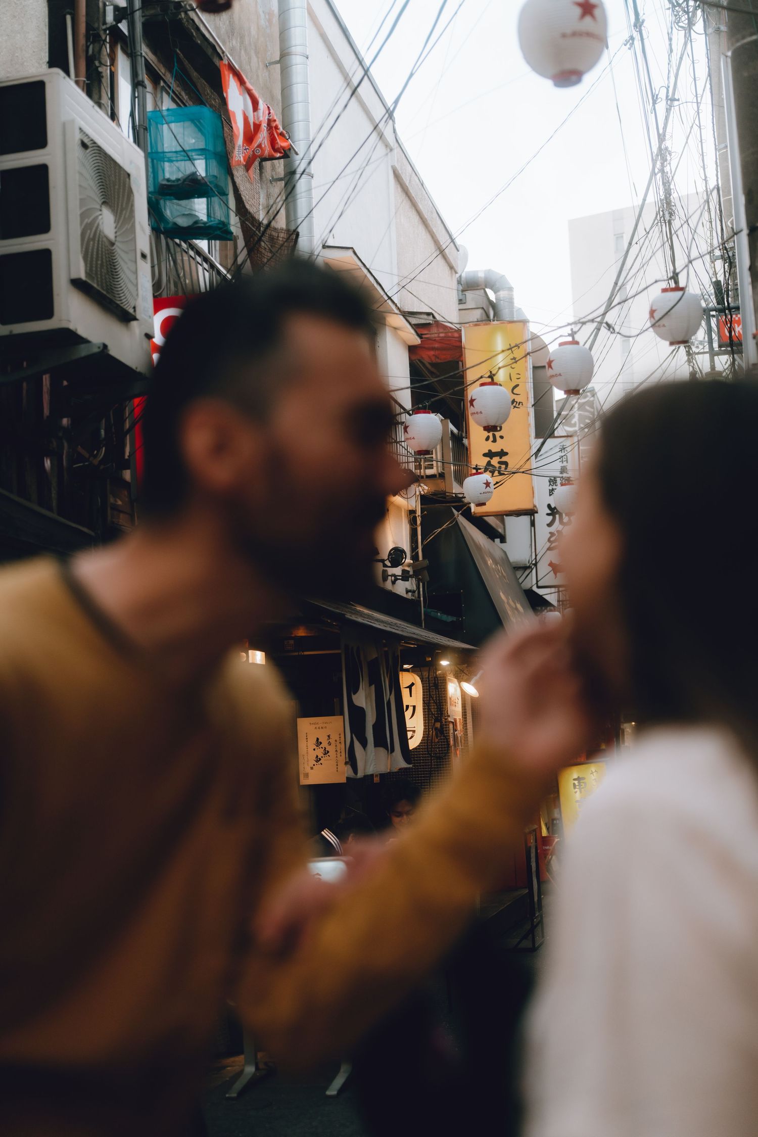 Couple standing close together in a narrow Japanese alley with lanterns and restaurant signs in the background.
