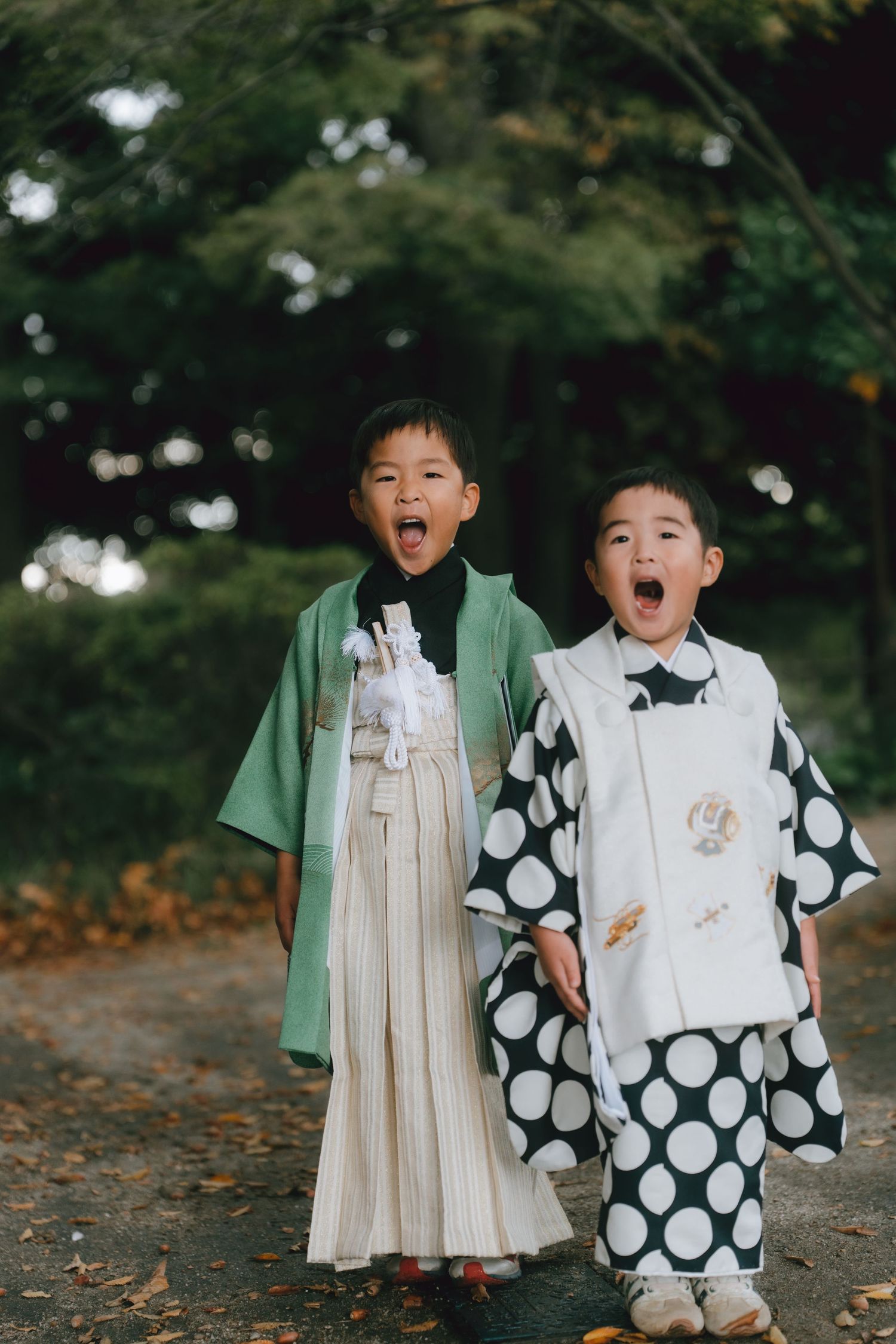 Two young boys in traditional Japanese kimono and hakama outfits walk together outdoors, mouths open in joyful expressions in Chiba SHRINE