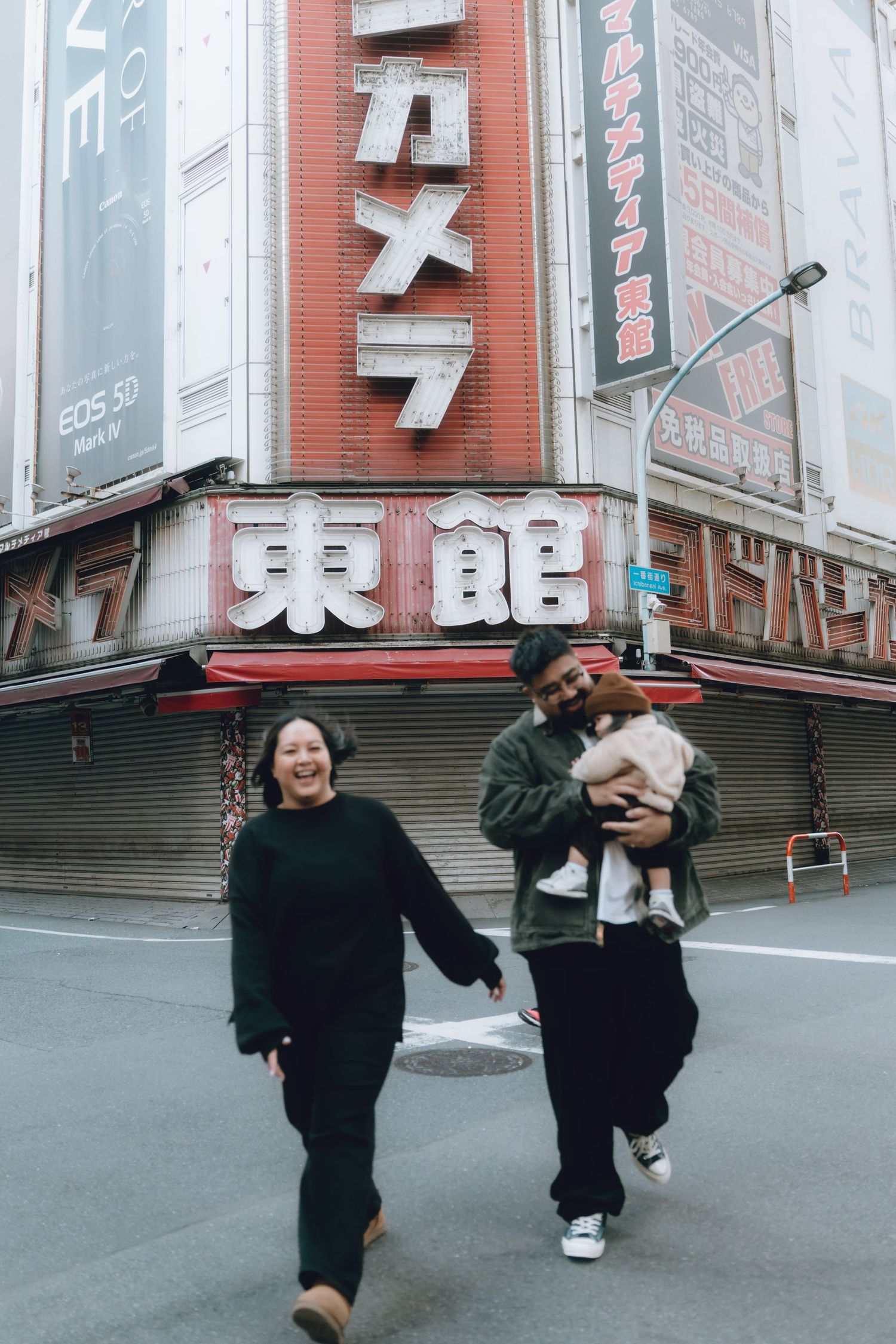 Couple holding hands and laughing with a small dog in front of a Japanese electronics store in Shinjyuku, Tokyo.