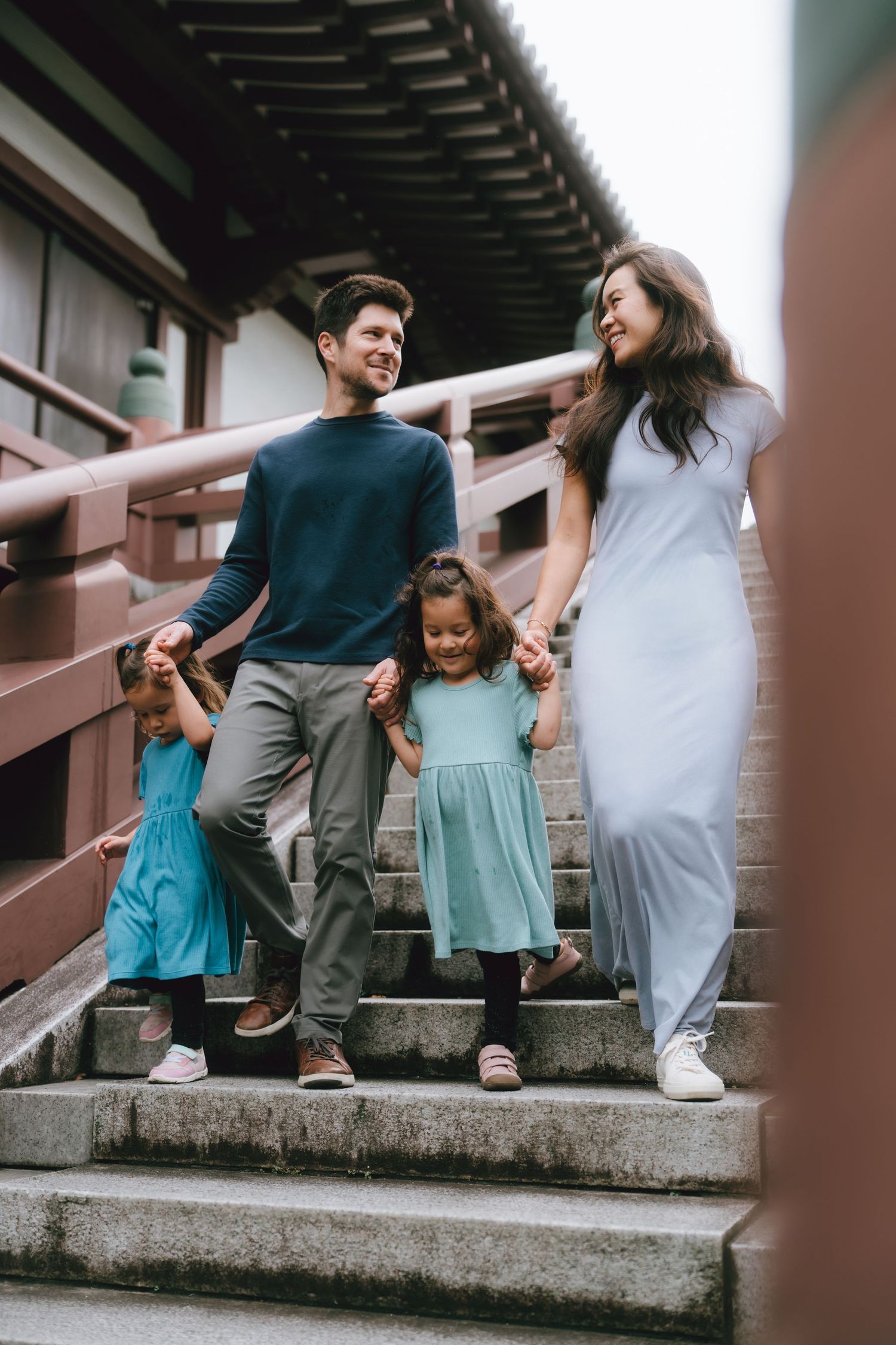 Happy mixed-race family of four holding hands on outdoor stairs in Zojoji, Tokyo. near Tokyo tower.