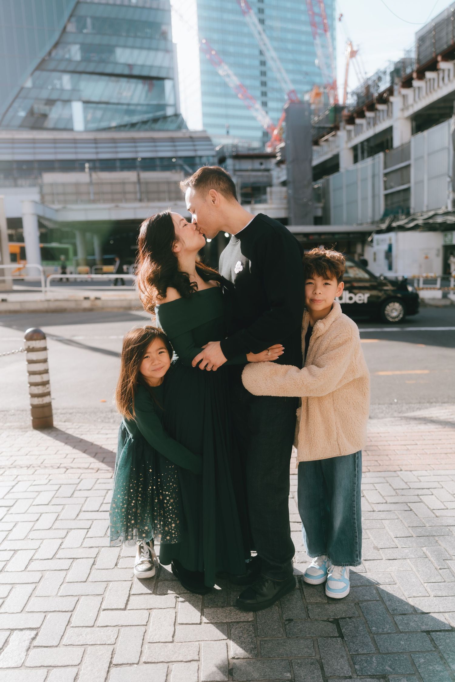 Family of four posing and kissing in front of modern SHIBUYA Tokyo skyscrapers on sunny day