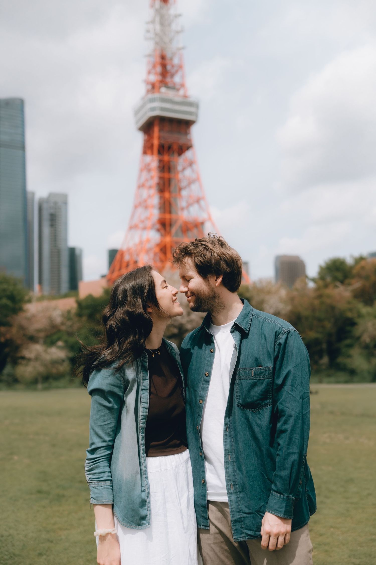 Couple sharing a romantic moment in front of Tokyo Tower on a cloudy day.