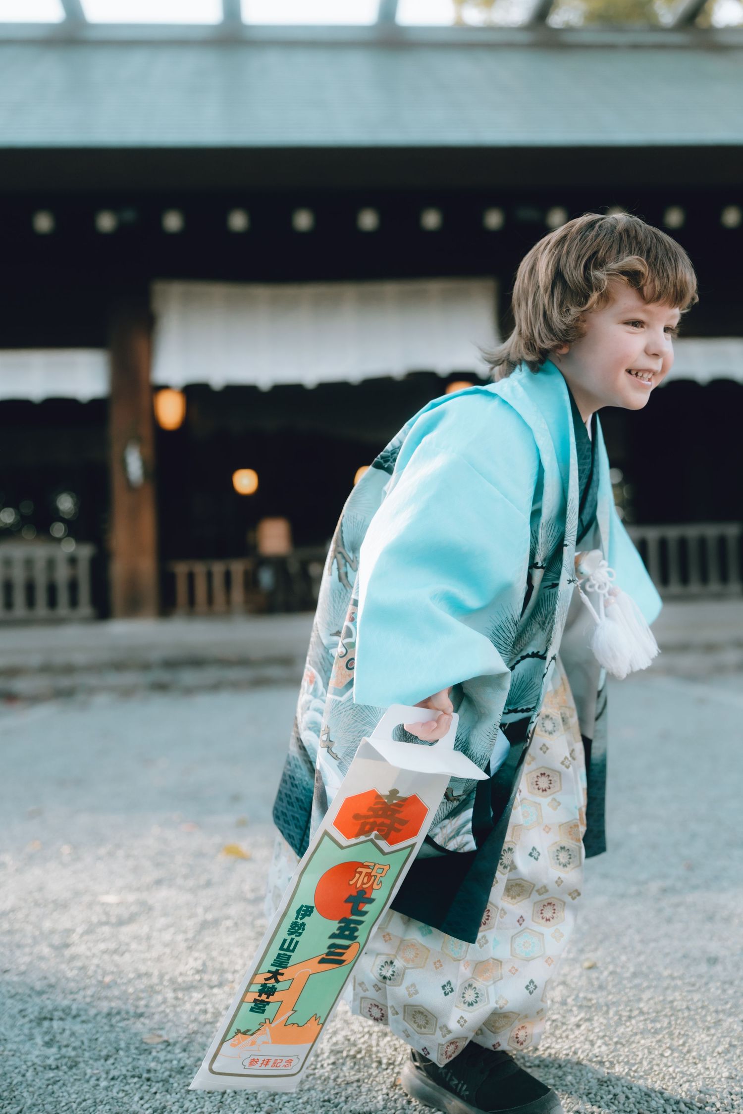 Young child wearing a traditional Japanese kimono at a yokohama shrine, smiling and walking on gravel path.