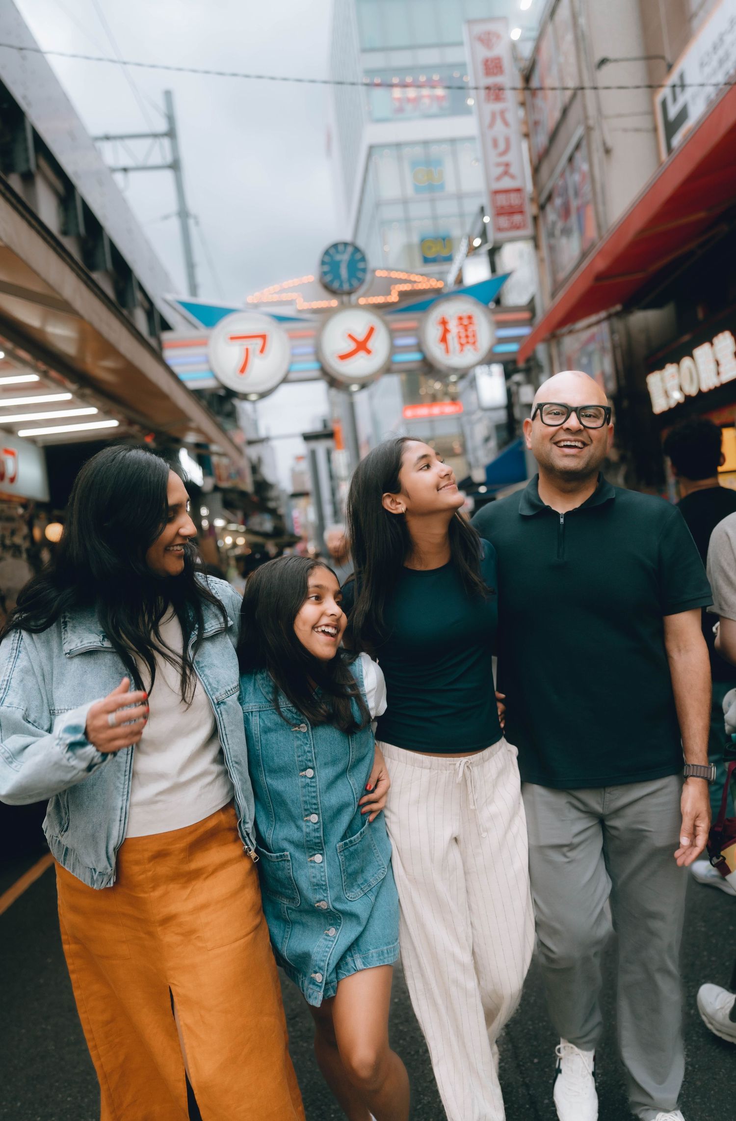 Happy family of four walking together at Ameyoko market street in Tokyo, Japan, smiling and embracing in Ueno, tokyo.