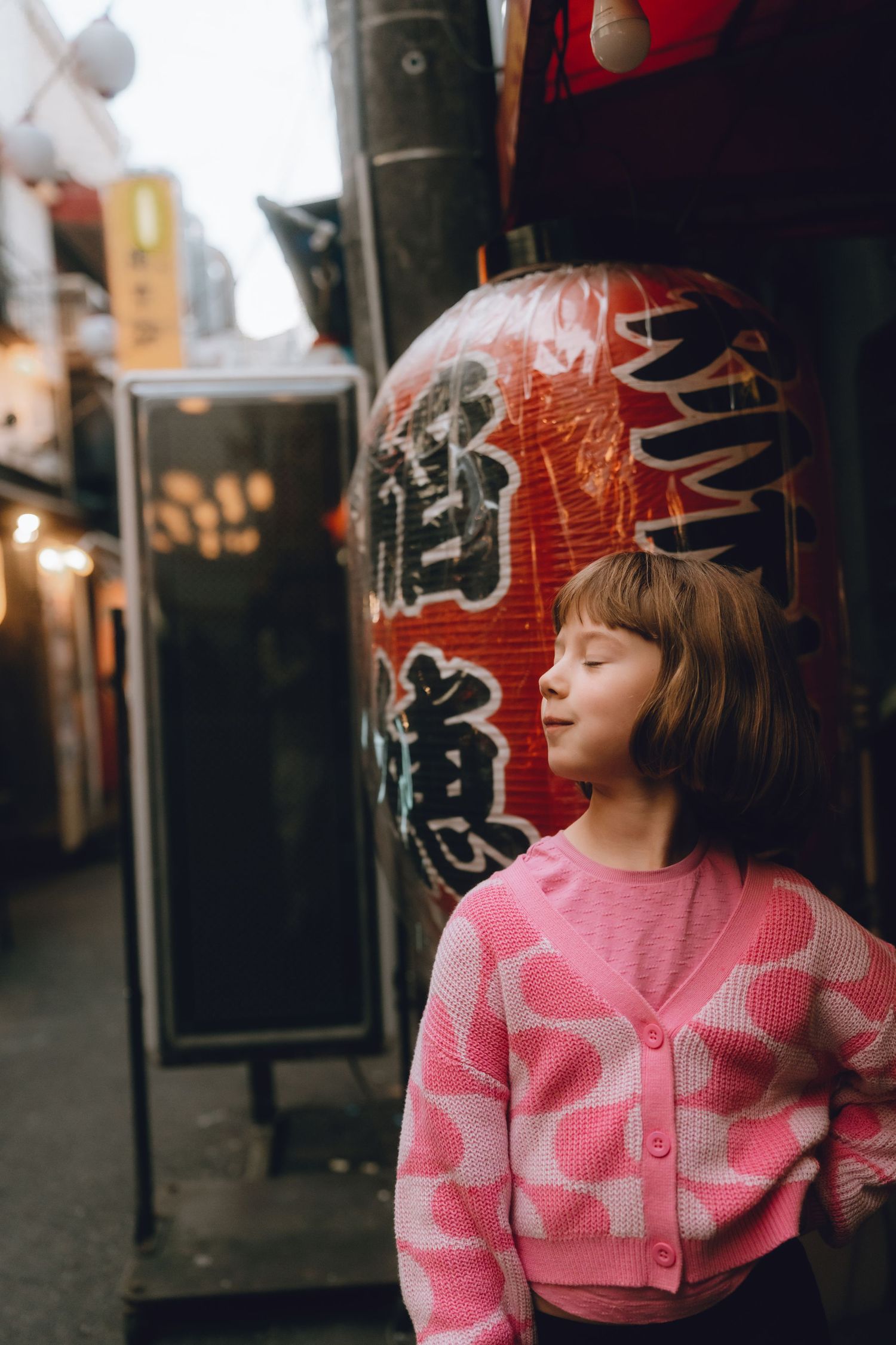 Young girl with eyes closed standing peacefully beside a large red Japanese paper lantern in tokyo.