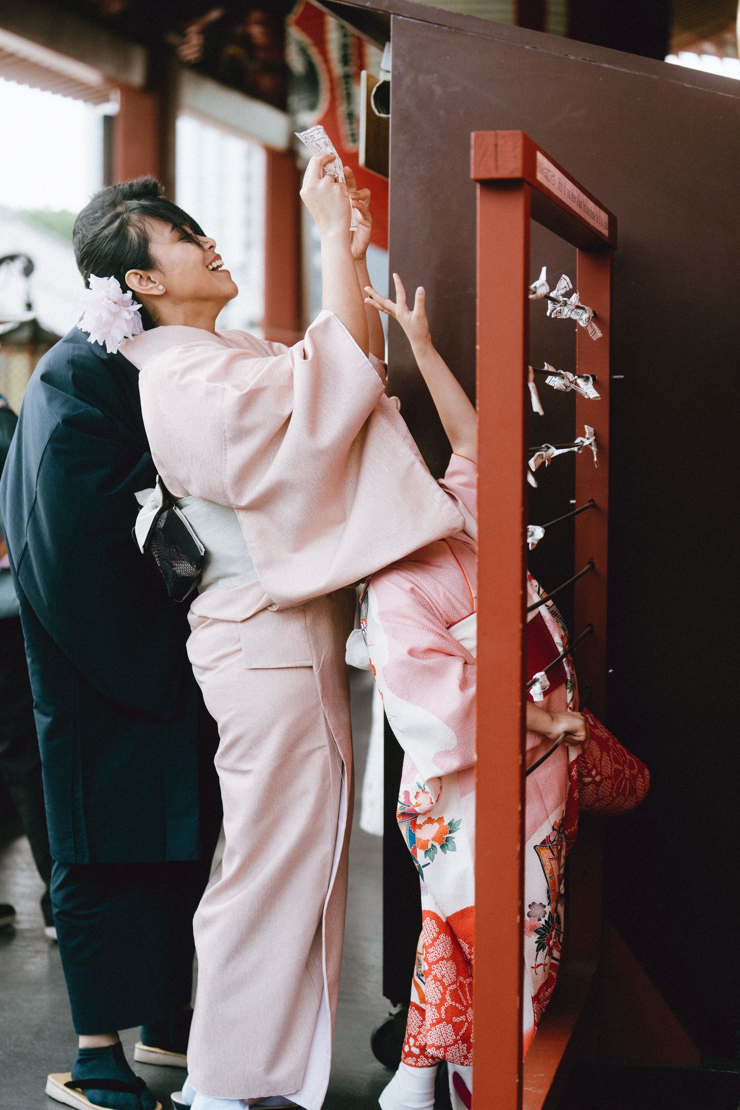 Women in pink kimonos attaching omikuji fortune papers to a red rack at Sensoji shrine Asakusa.