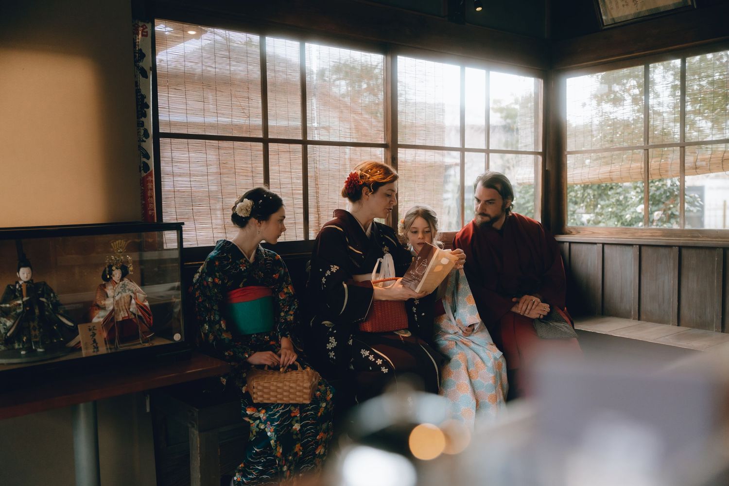 Family in traditional Japanese kimonos gathered indoors, examining items together near decorative dolls display.Sawara, Chiba, Japan.